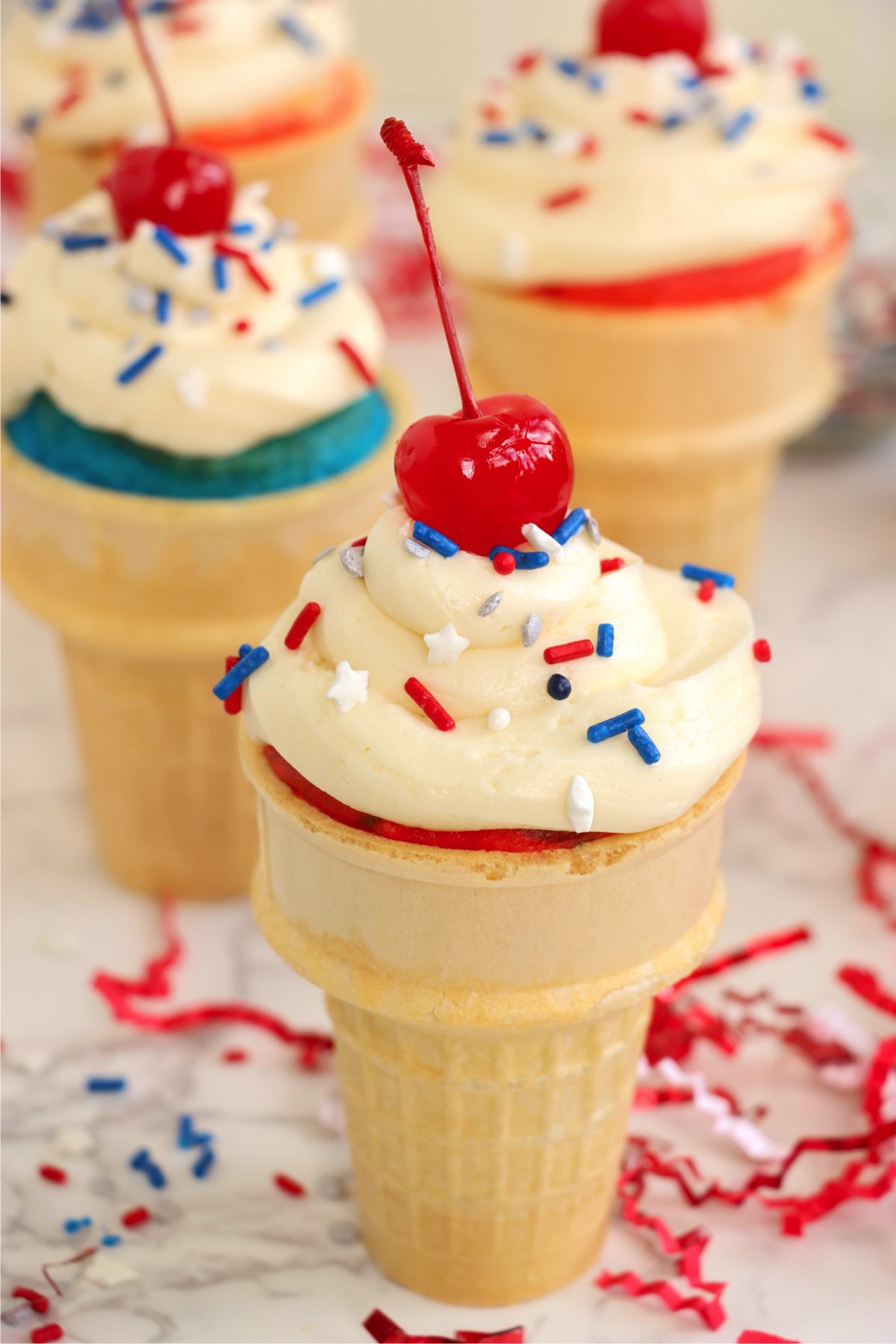 Frosted cupcake cone topped with red, white, and blue sprinkles and a cherry.