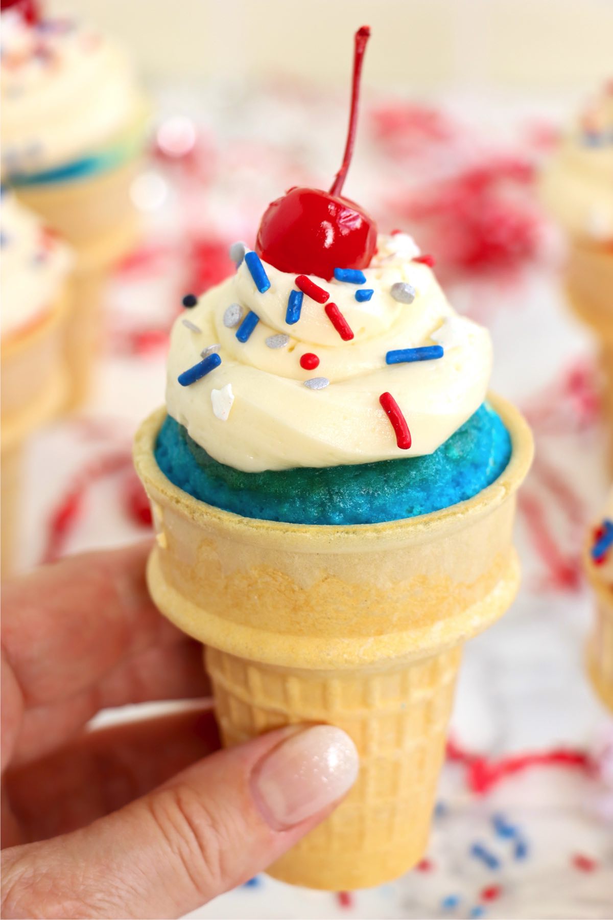 Blue cupcake cone held up close with swirled frosting and a cherry.