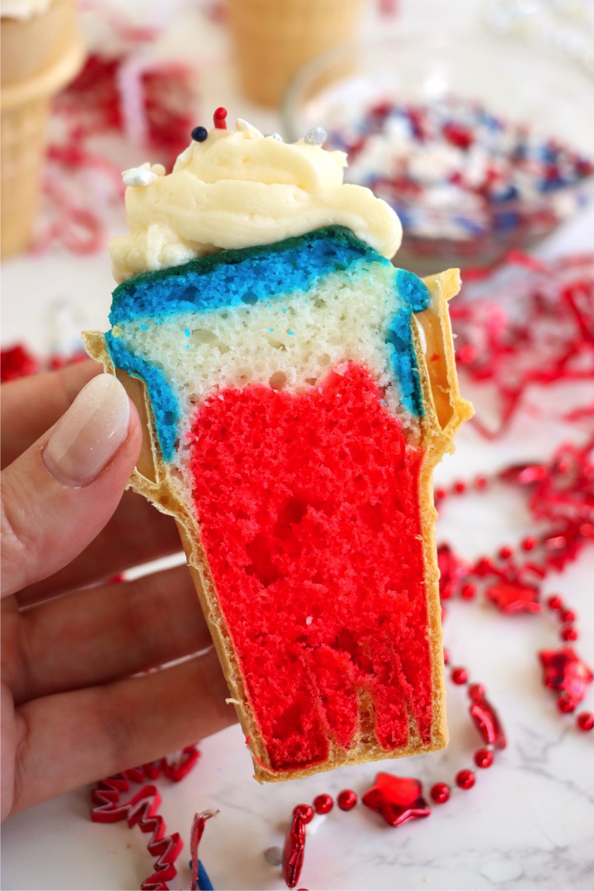 Hand holding a sliced cupcake cone, revealing colorful cake layers and frosting.