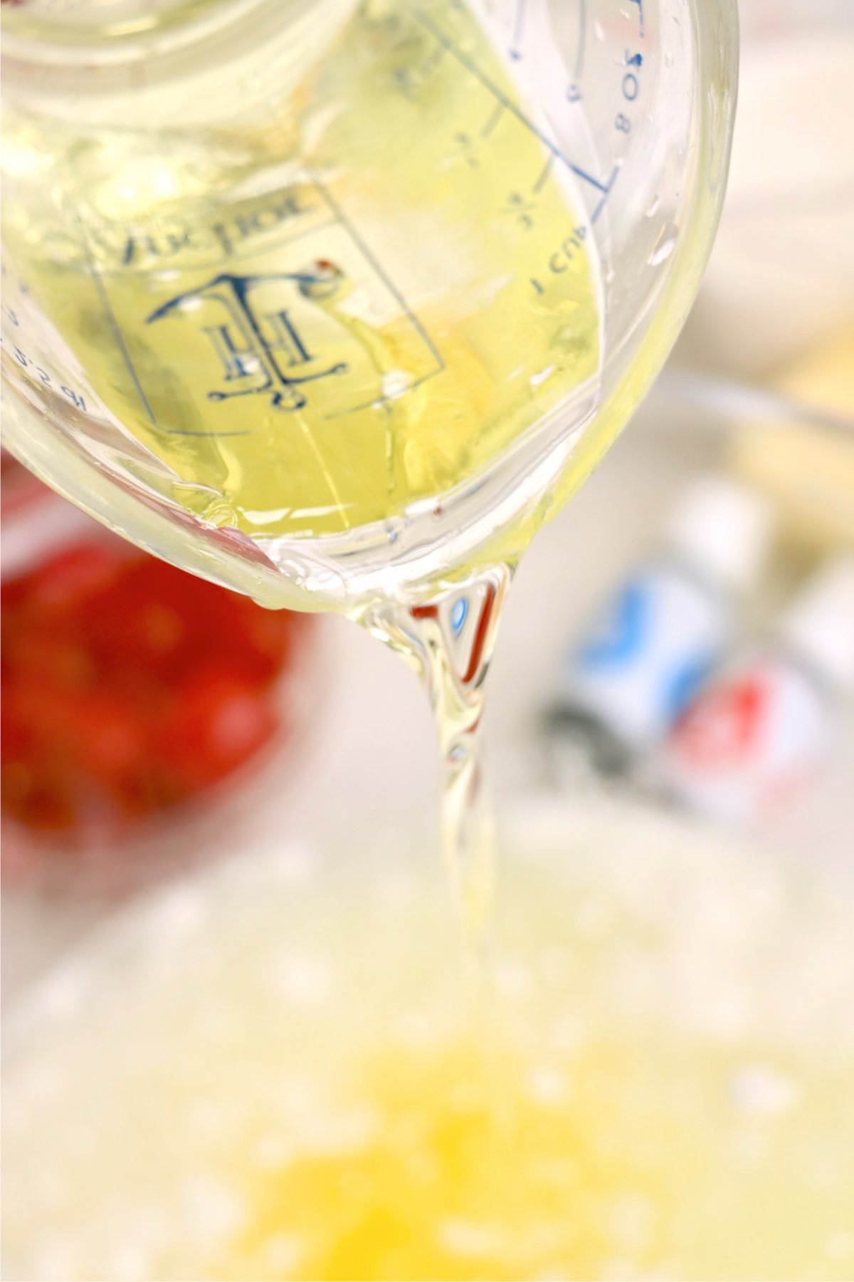 Measuring cup with oil being poured into a mixing bowl.