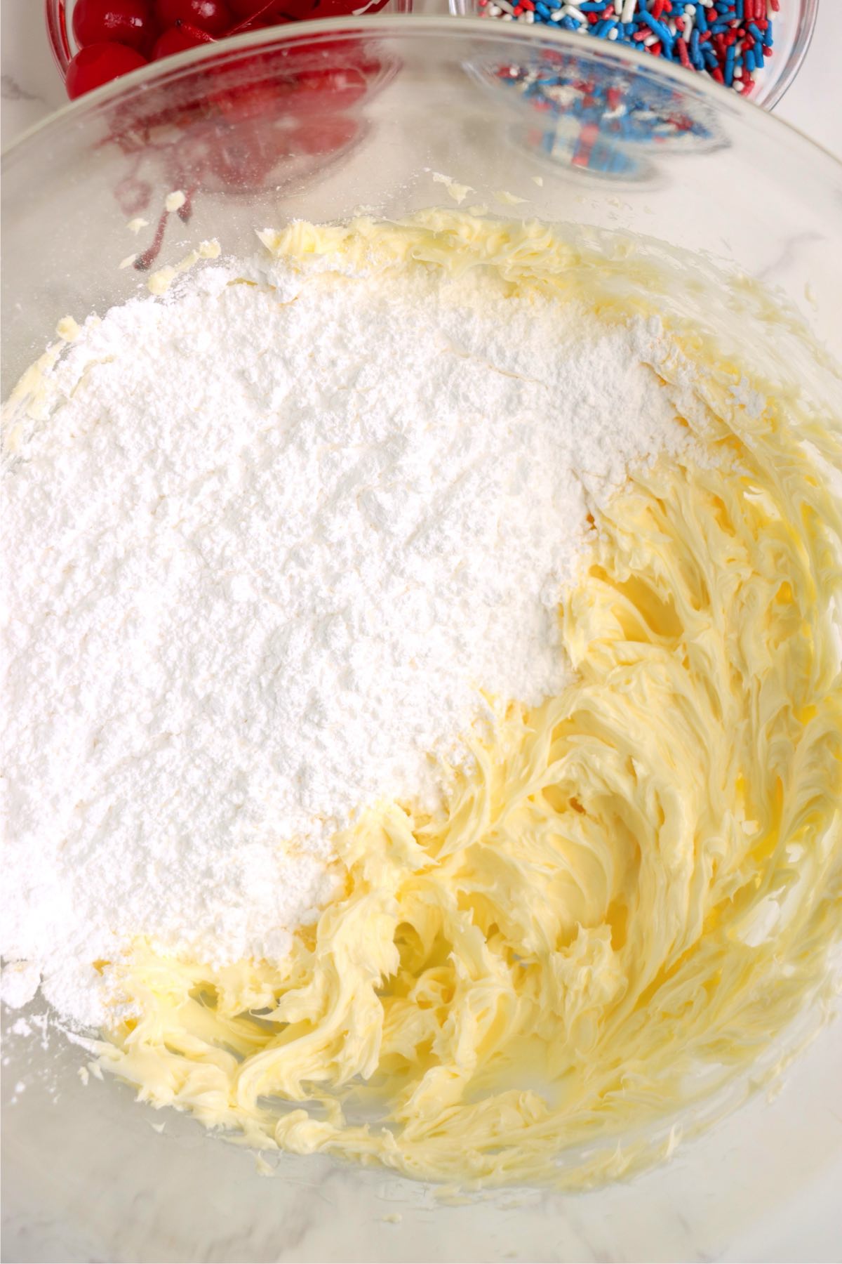Butter and powdered sugar being mixed together in a large glass bowl.