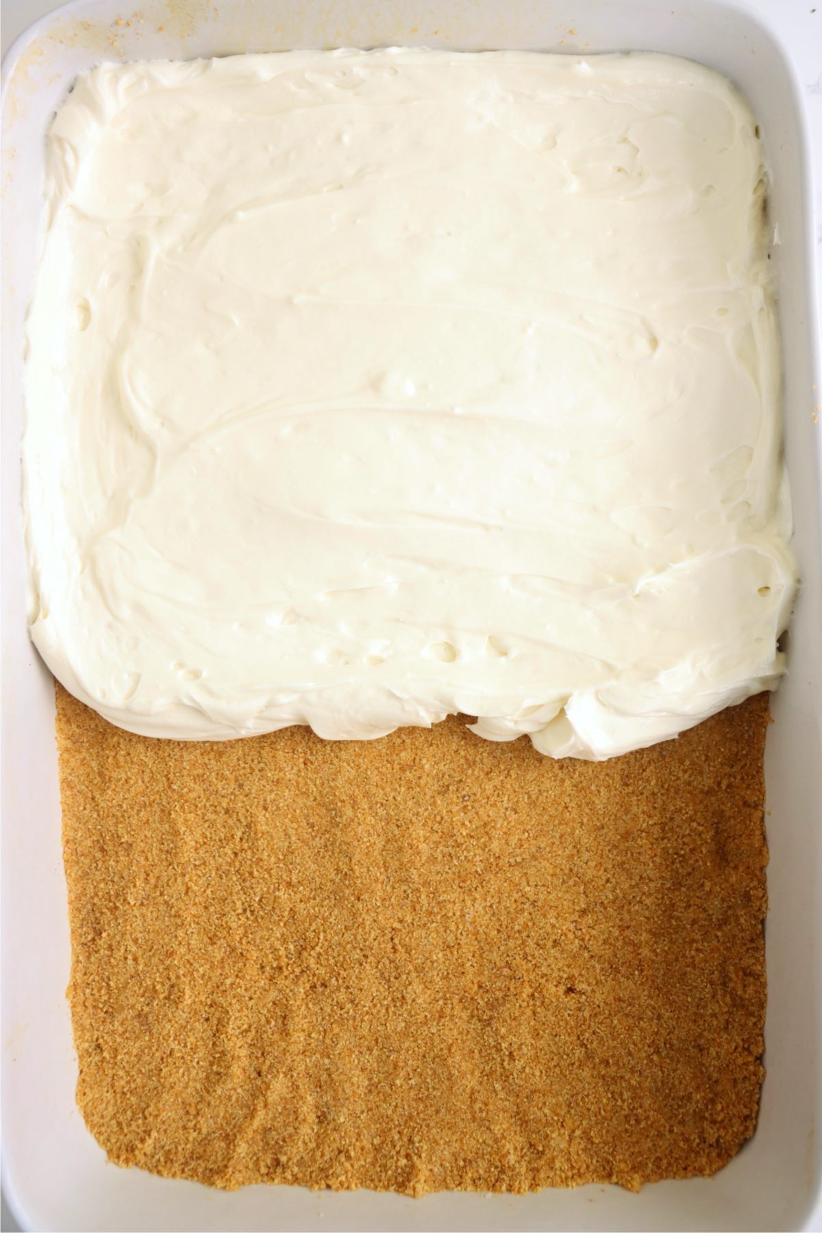 Smooth cheesecake filling being spread evenly over the crust in a baking dish.