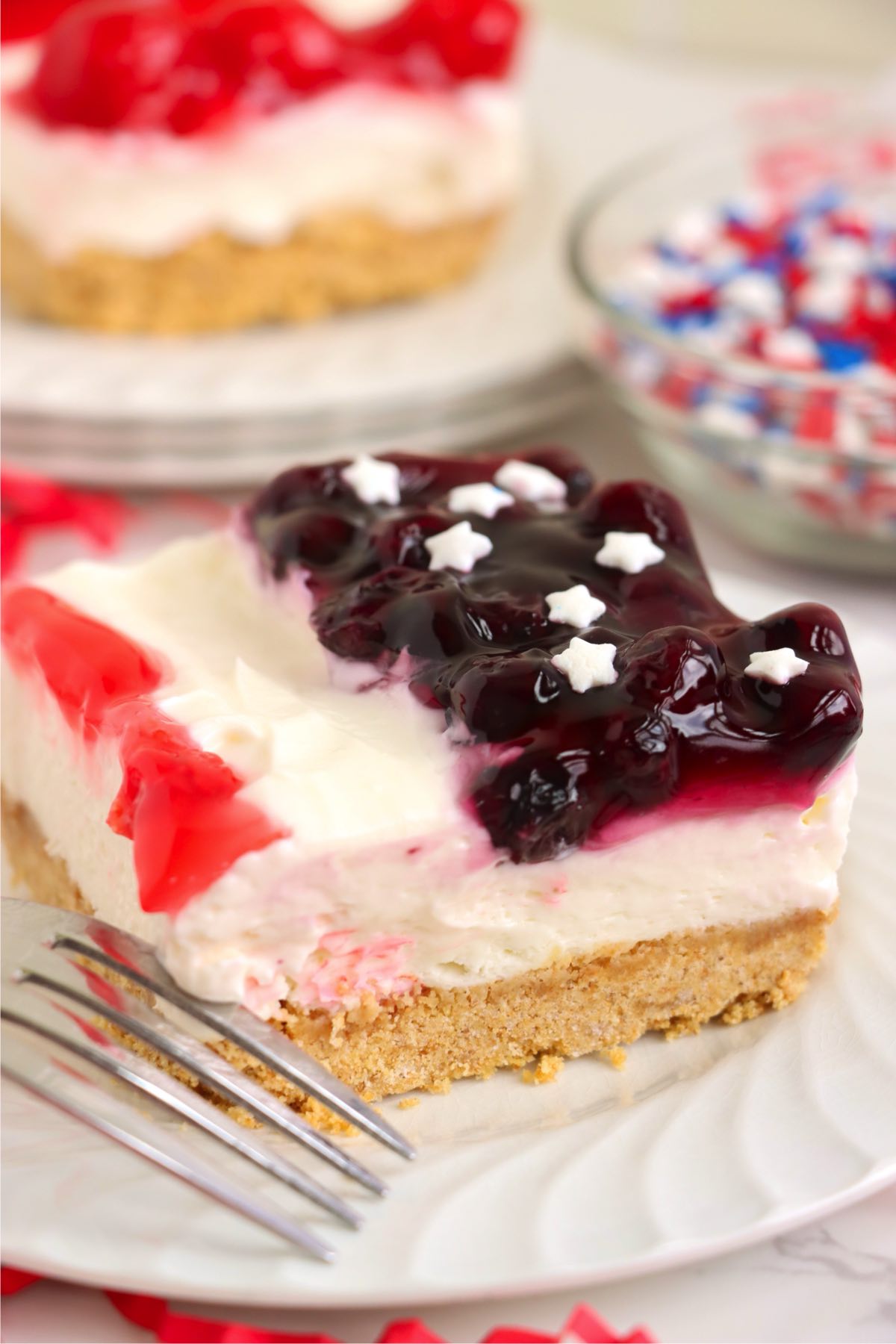 Plated red white and blue cheesecake slice arranged on a white surface.