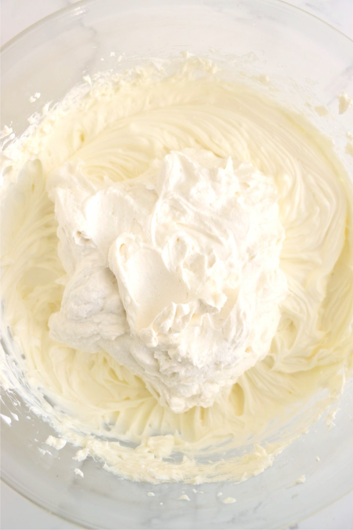 Cream cheese, sugar, and sour cream being mixed with a hand mixer in a white bowl.