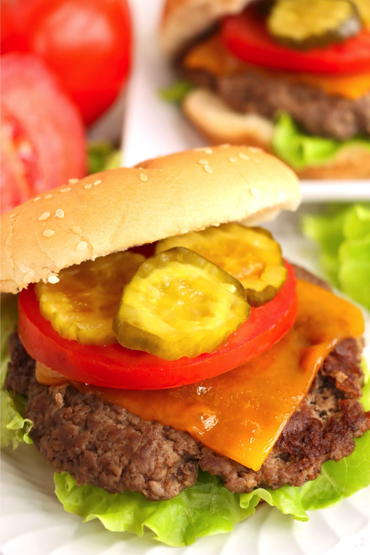 Assembled cheeseburger with lettuce, cheddar, tomato, and pickles.