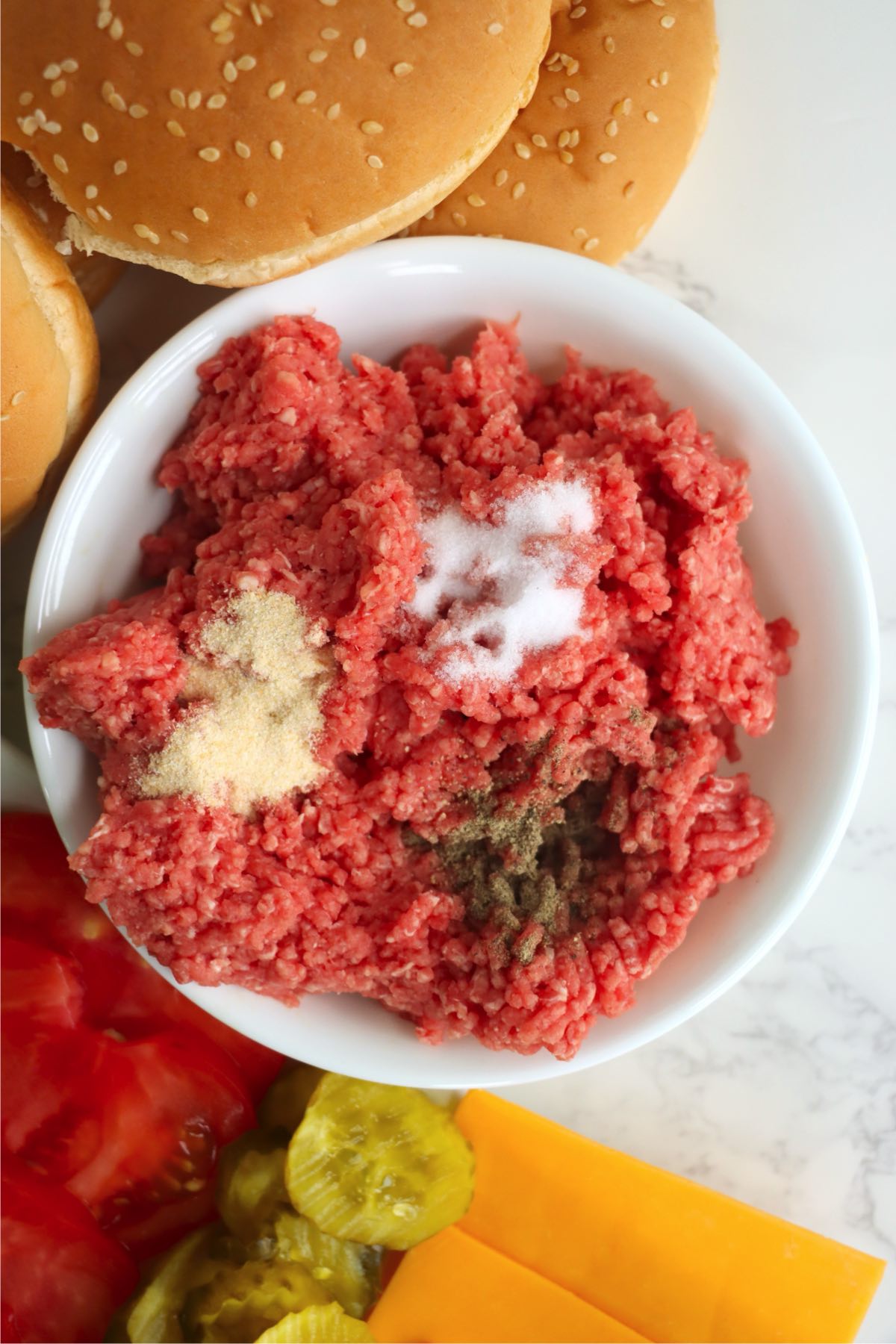 Ground beef in a bowl topped with salt, pepper, and onion powder.