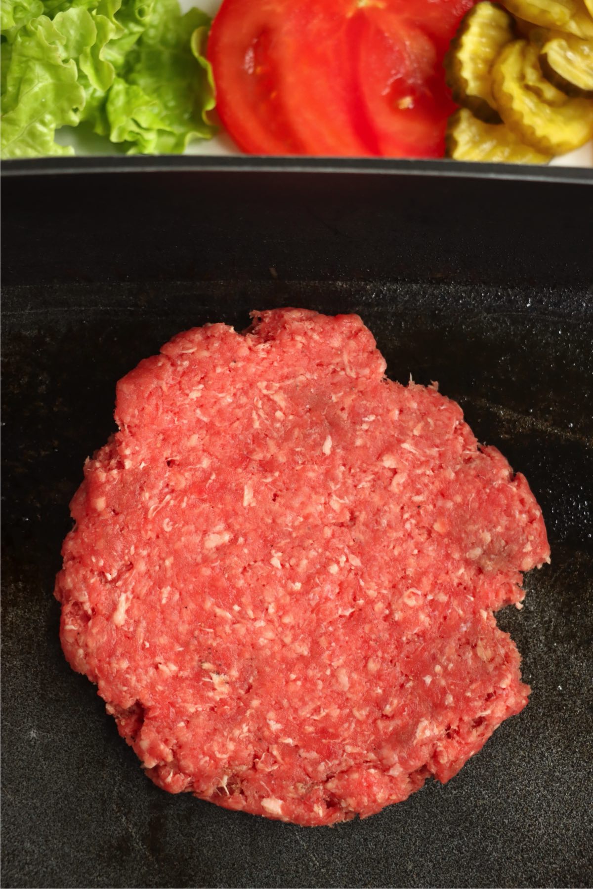 Flattened raw burger patty on a griddle pan.