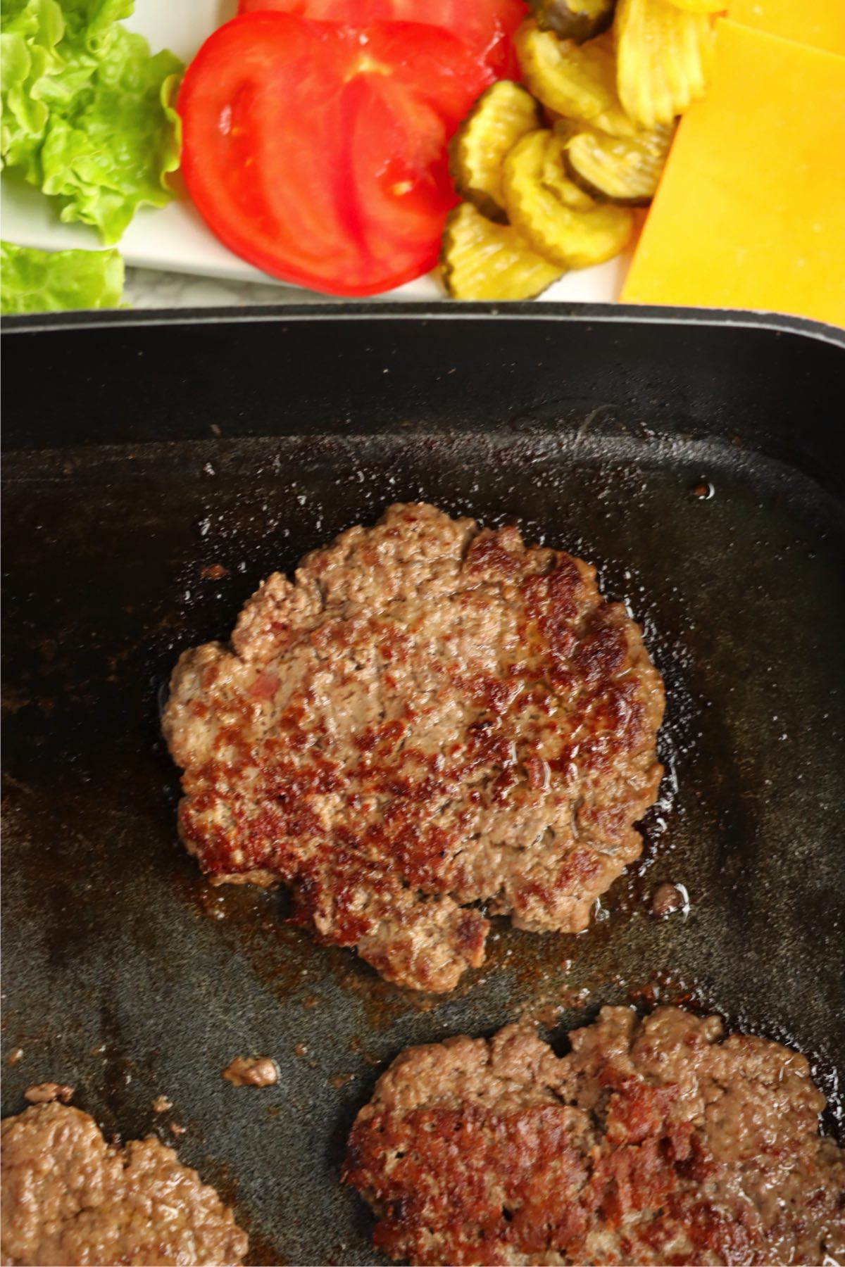 Three beef patties cooking on a griddle with browned edges.