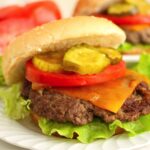 Cheeseburger with lettuce, tomato, pickles, and cheddar on a sesame bun.