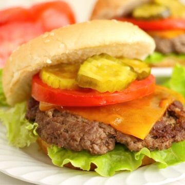 Cheeseburger with lettuce, tomato, pickles, and cheddar on a sesame bun.