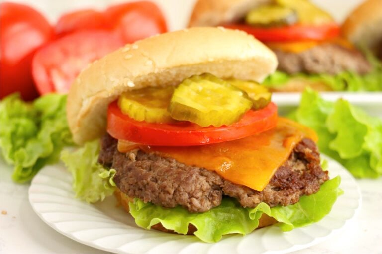 Cheeseburger with lettuce, tomato, pickles, and cheddar on a sesame bun.