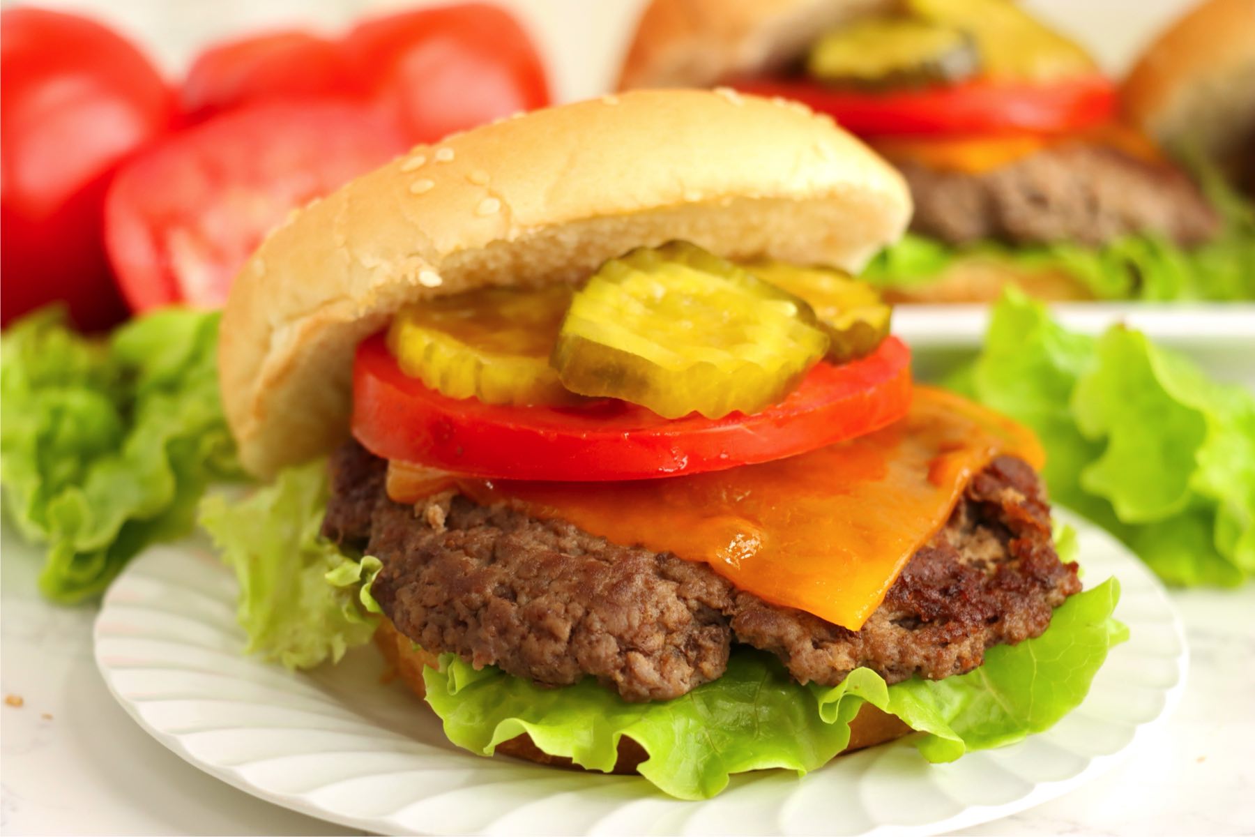 Cheeseburger with lettuce, tomato, pickles, and cheddar on a sesame bun.
