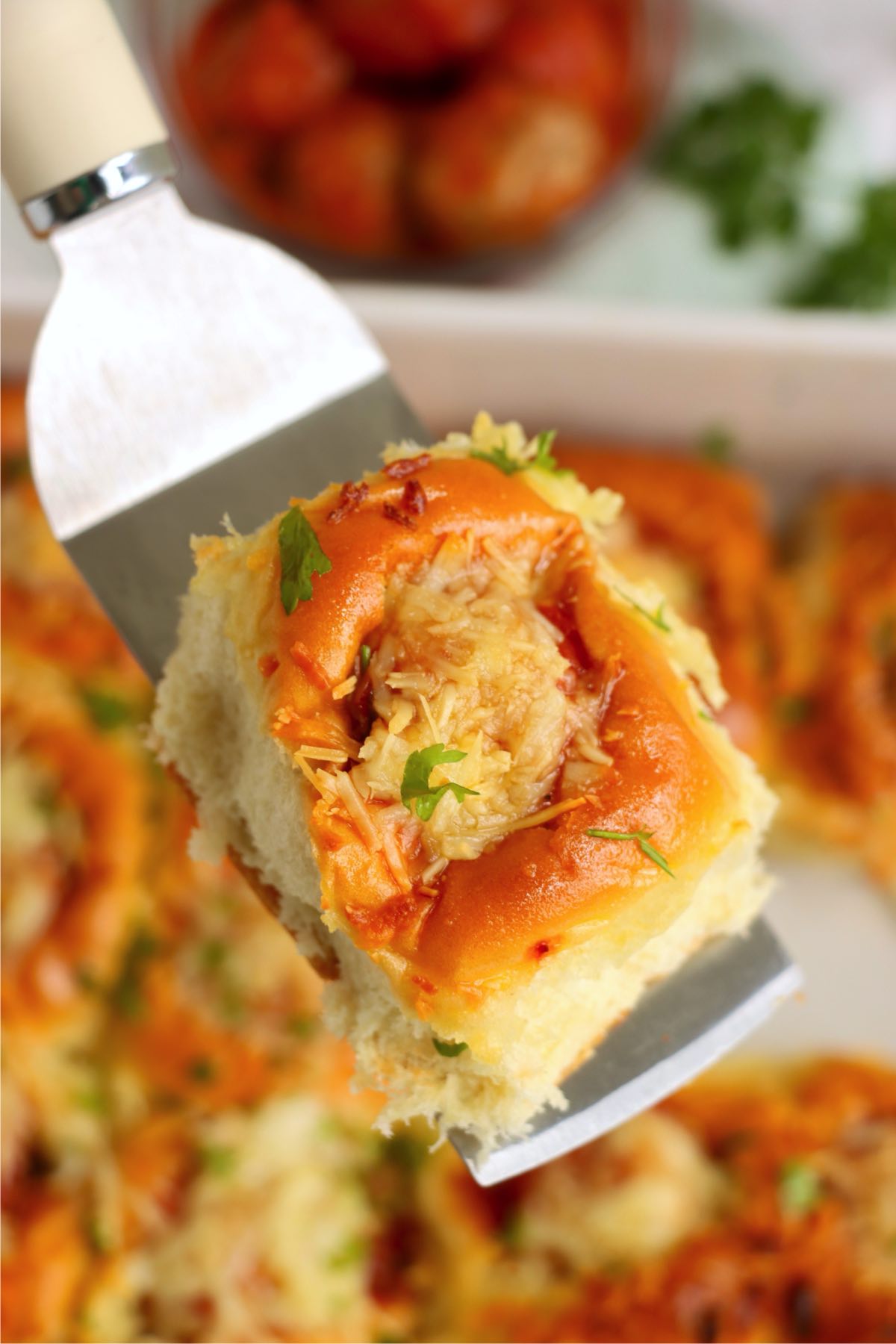 A single slider being lifted from the baking dish with a spatula, showing its golden top and cheesy center.