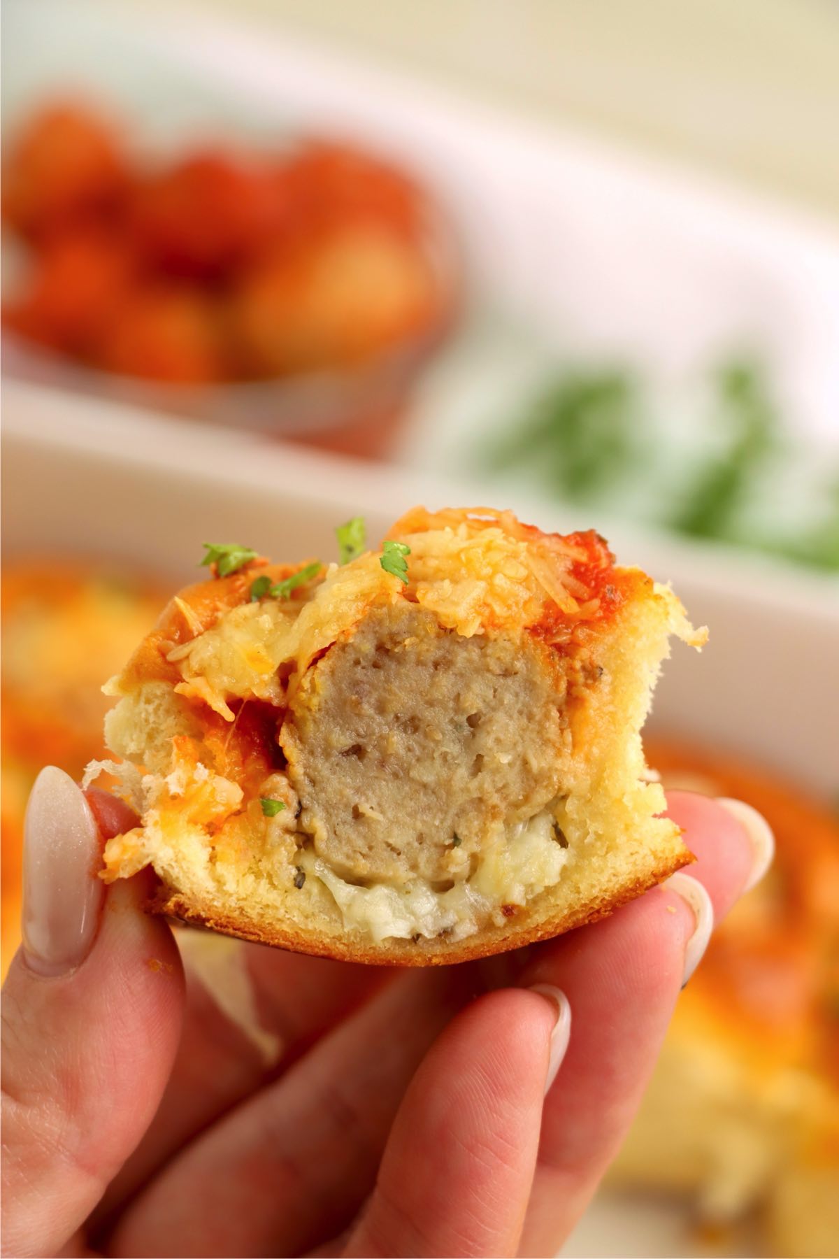A half-eaten slider held in hand, revealing a meatball center surrounded by melted cheese and soft bread.