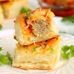 Stacked sliders on a white plate with fresh parsley garnish and a blurred background of more sliders.