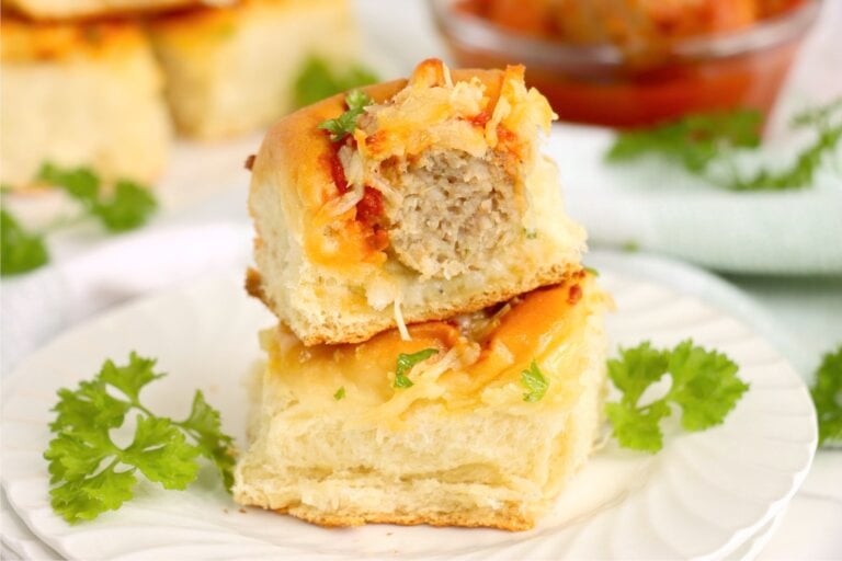 Stacked sliders on a white plate with fresh parsley garnish and a blurred background of more sliders.