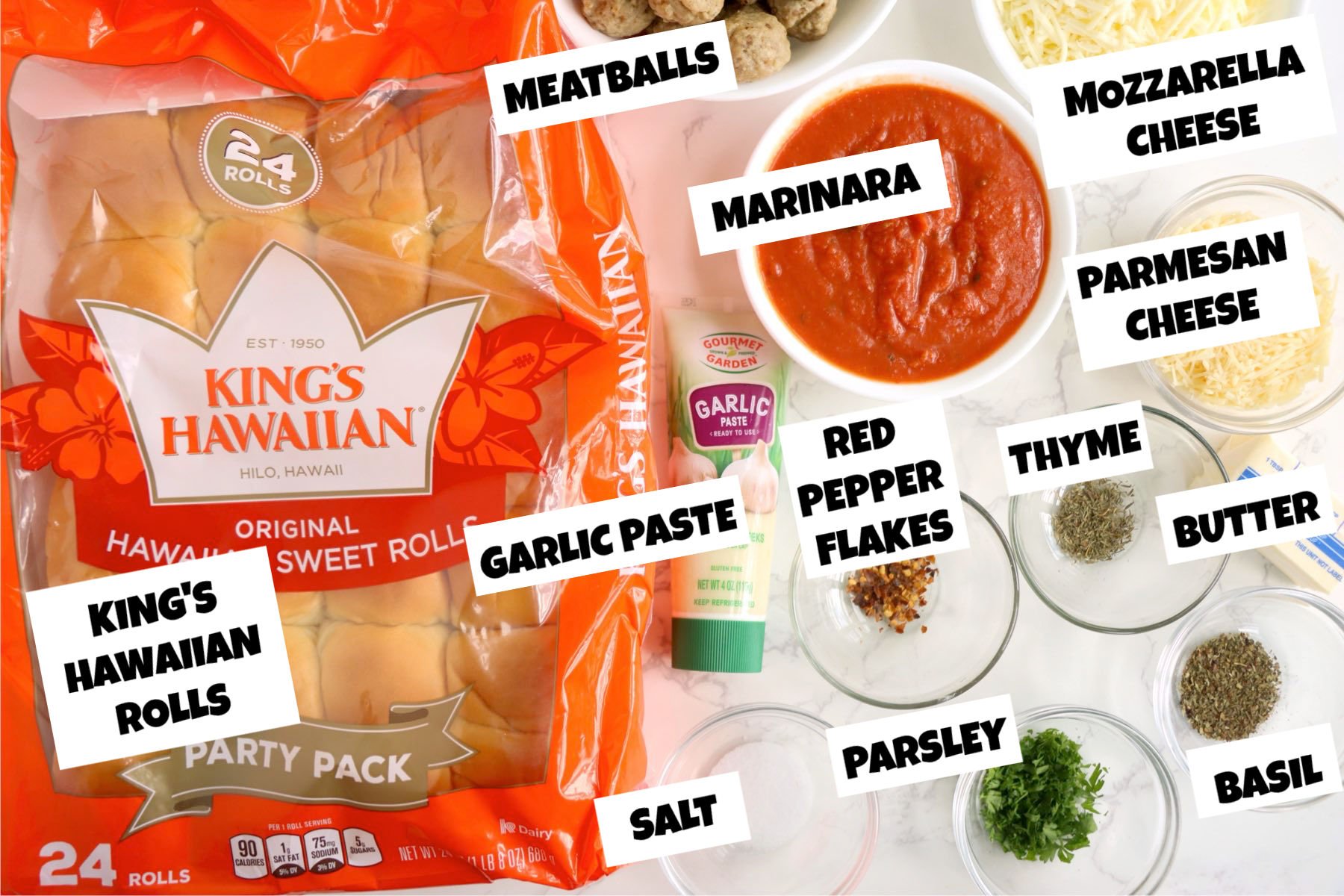 Hawaiian rolls, marinara, garlic paste, herbs, cheese, and meatballs arranged on a white surface.