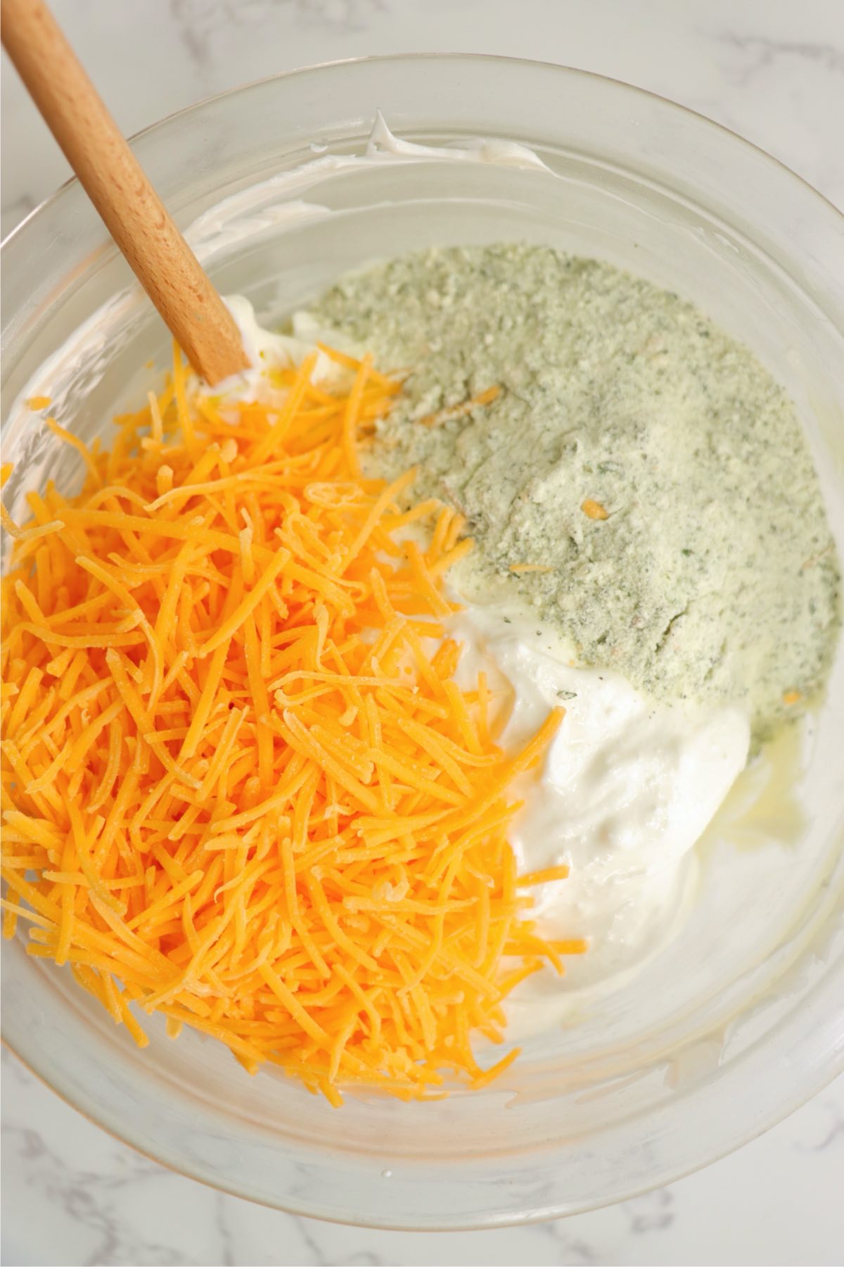 Cheddar cheese, ranch seasoning, and sour cream in a mixing bowl, ready to be blended.