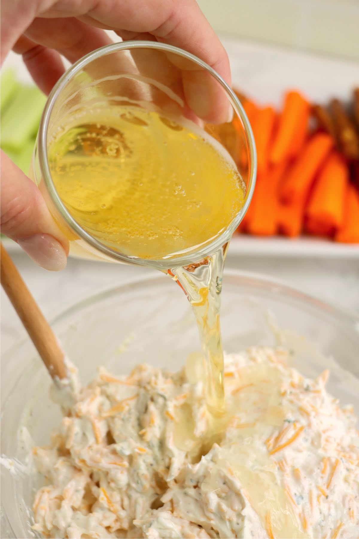 Beer being poured into the dip mixture in a glass bowl.