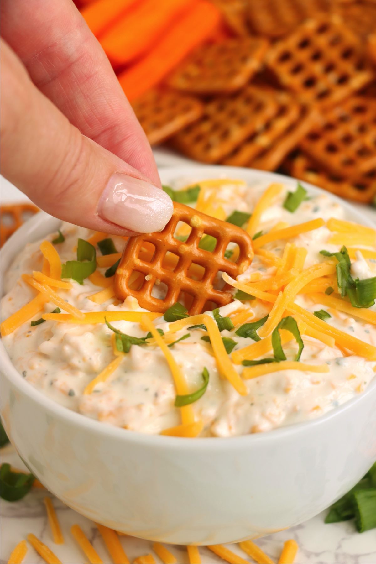 Fingers dipping a pretzel into creamy ranch beer dip.