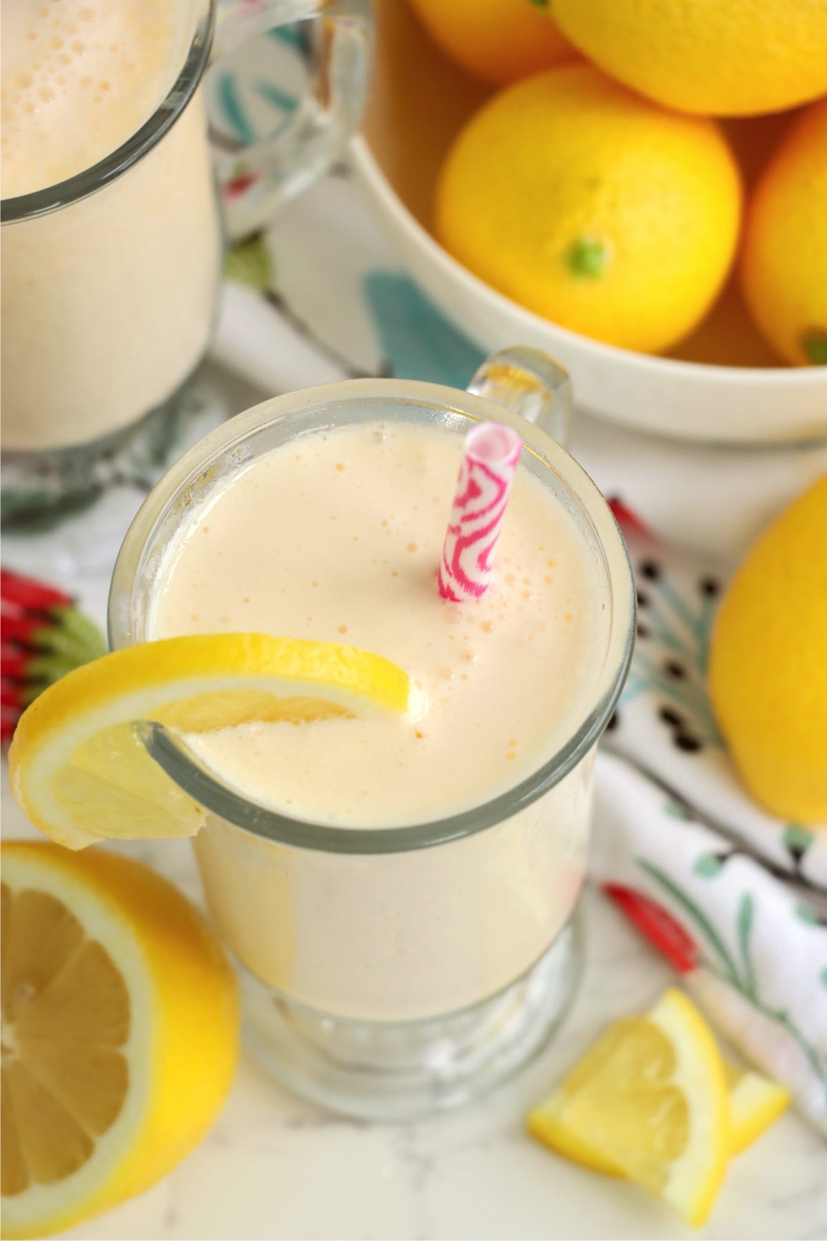 Overhead view of two frosted lemonades in glass mugs with lemon wedges and a bowl of whole lemons in the background.