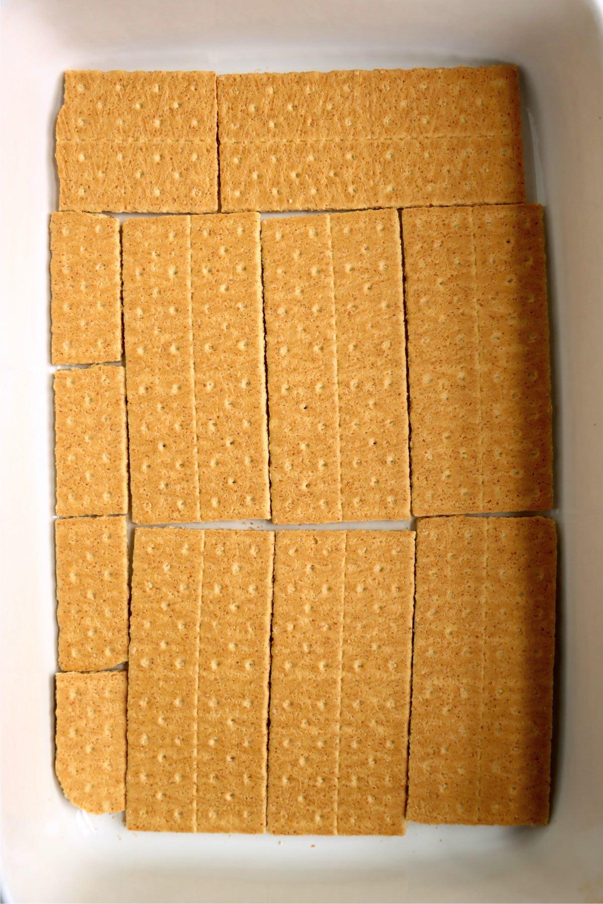 A layer of golden graham crackers neatly arranged in the bottom of a white rectangular baking dish.