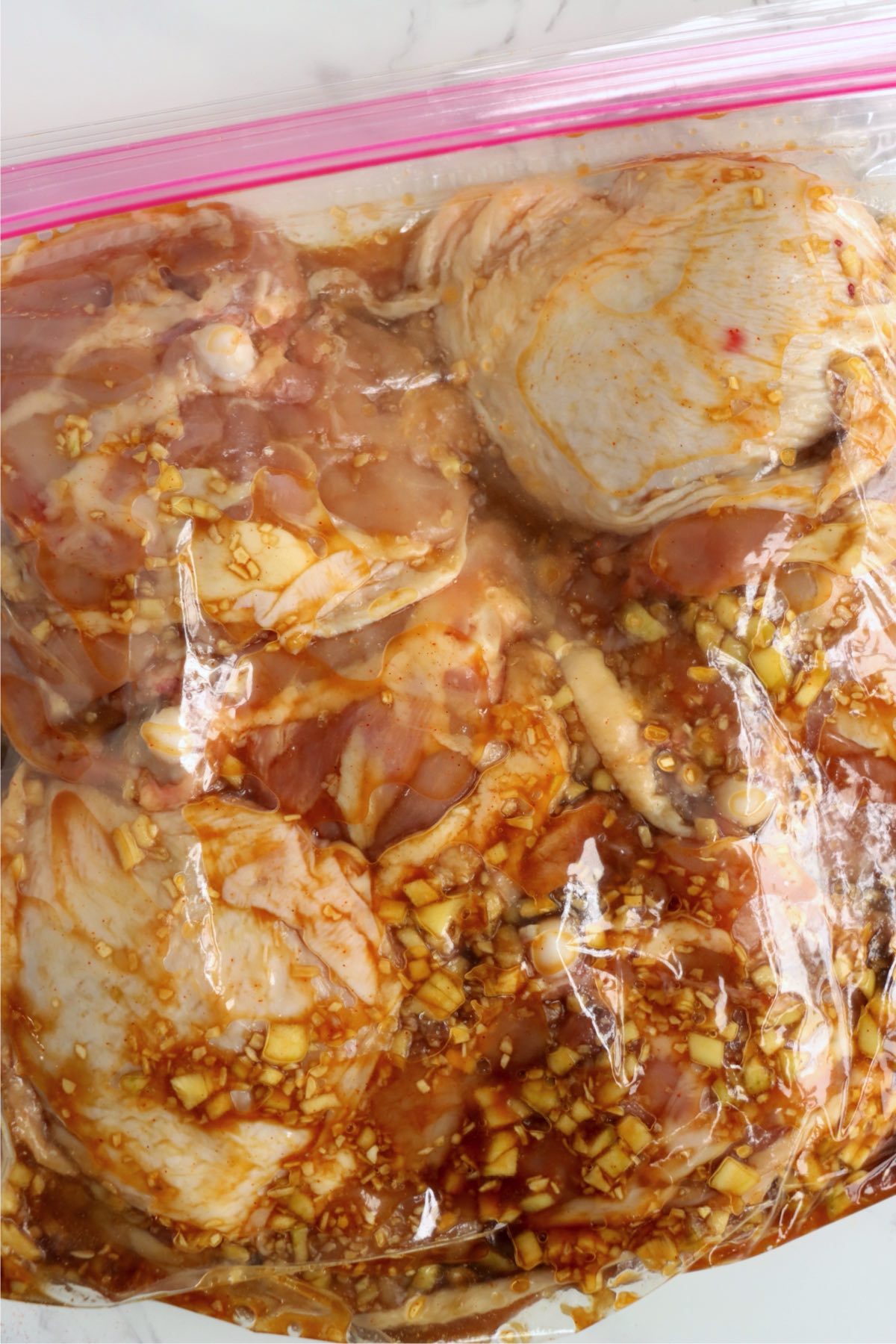 Chicken thighs soaking in a marinade inside a sealed ziplock bag, fully coated and ready to refrigerate.