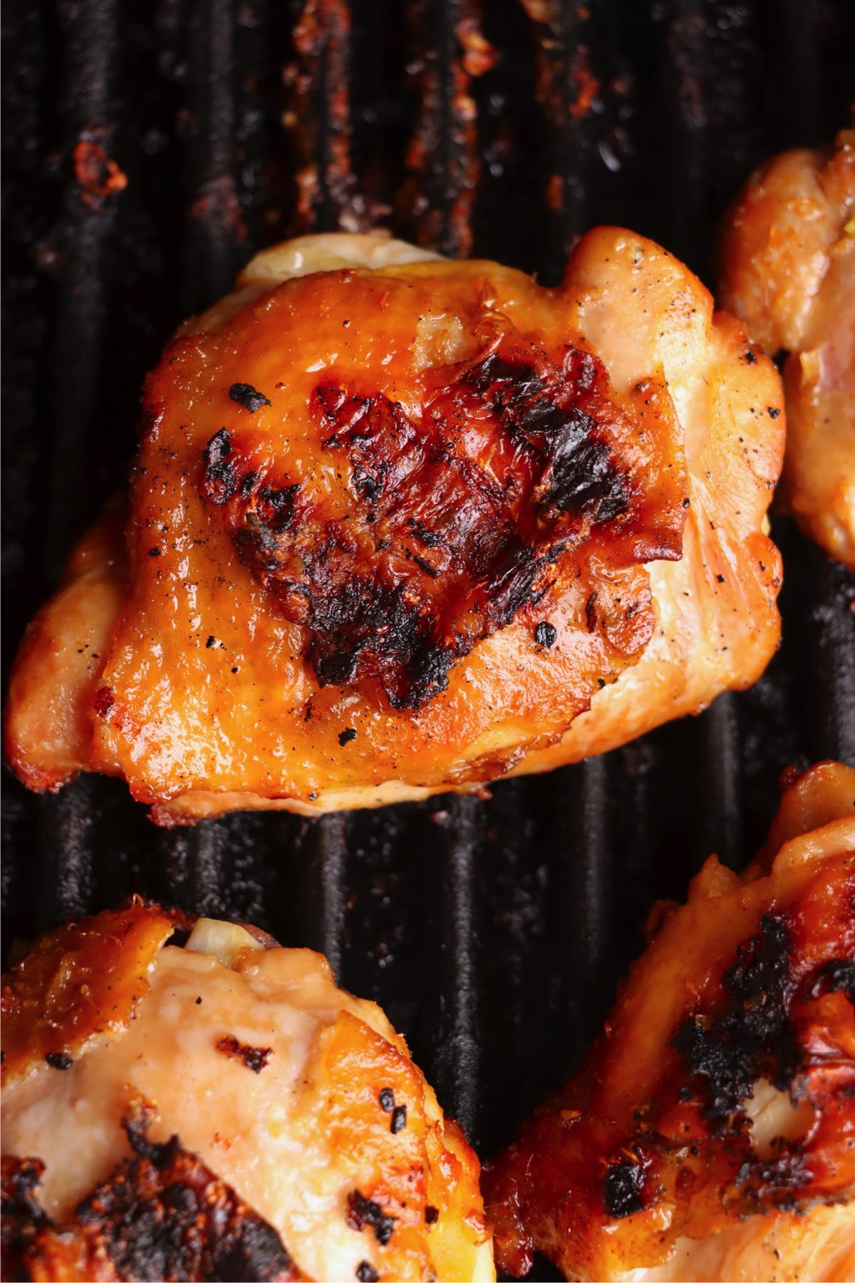 Grilled chicken thighs developing a golden color and char marks as they cook on the grill.