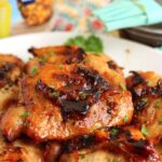 Grilled chicken thighs on a serving plate, with a marinade brush and pineapple juice container in the background.