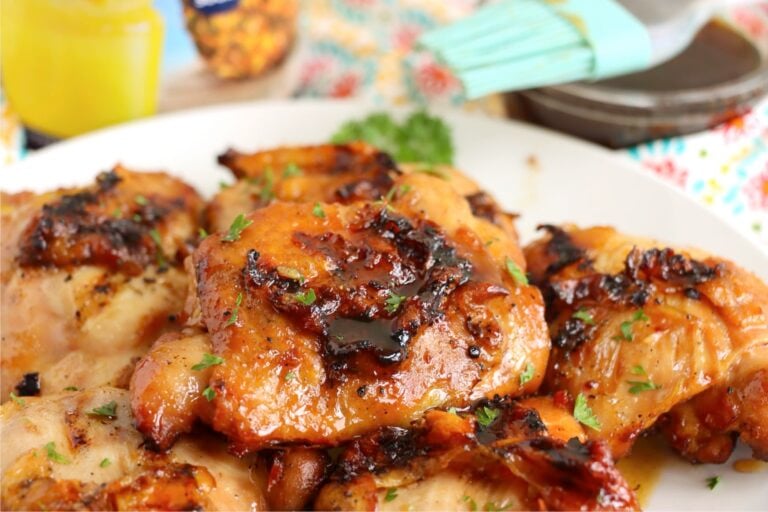 Grilled chicken thighs on a serving plate, with a marinade brush and pineapple juice container in the background.