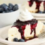 A slice of pie with blueberry sauce and whipped topping next to a bowl of fresh blueberries.