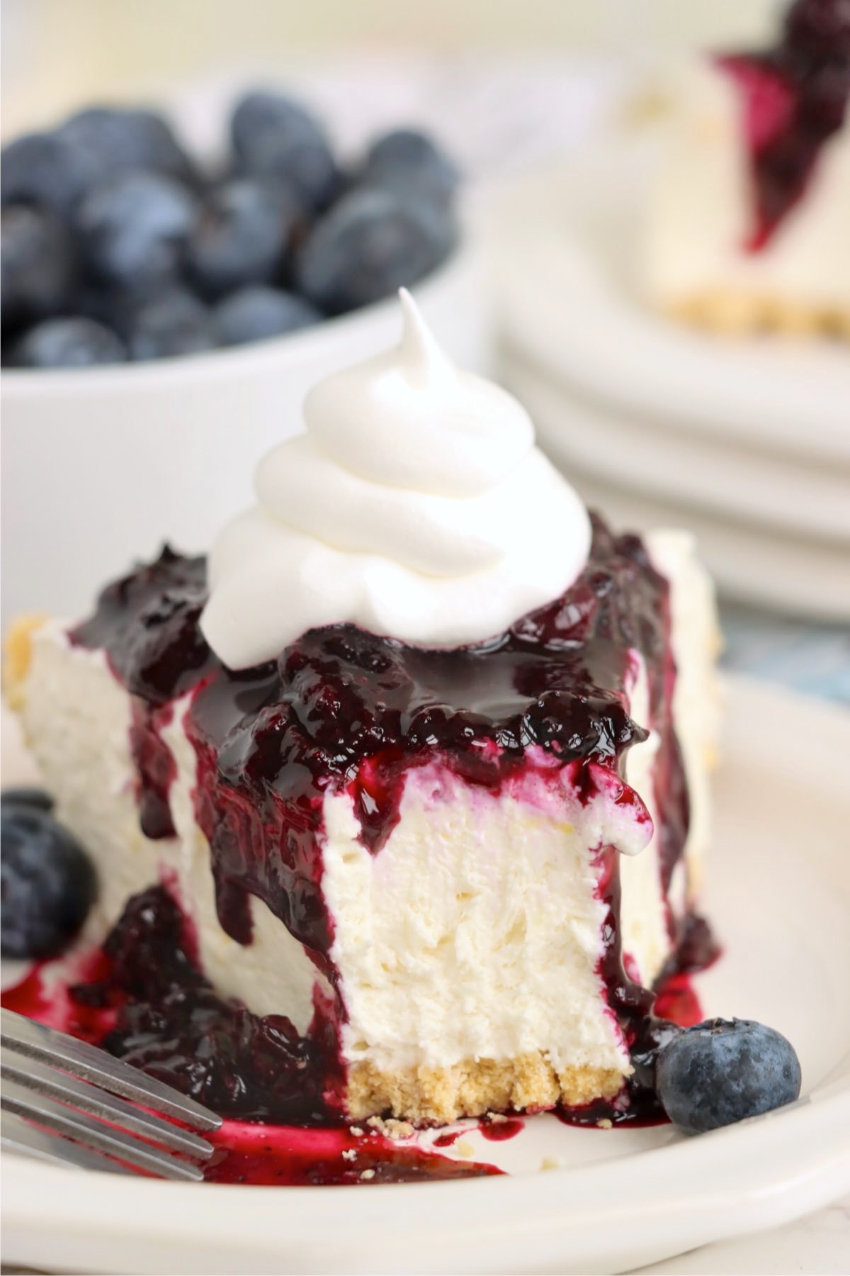 Close-up of a slice of pie with blueberry sauce and whipped topping and a bite missing.