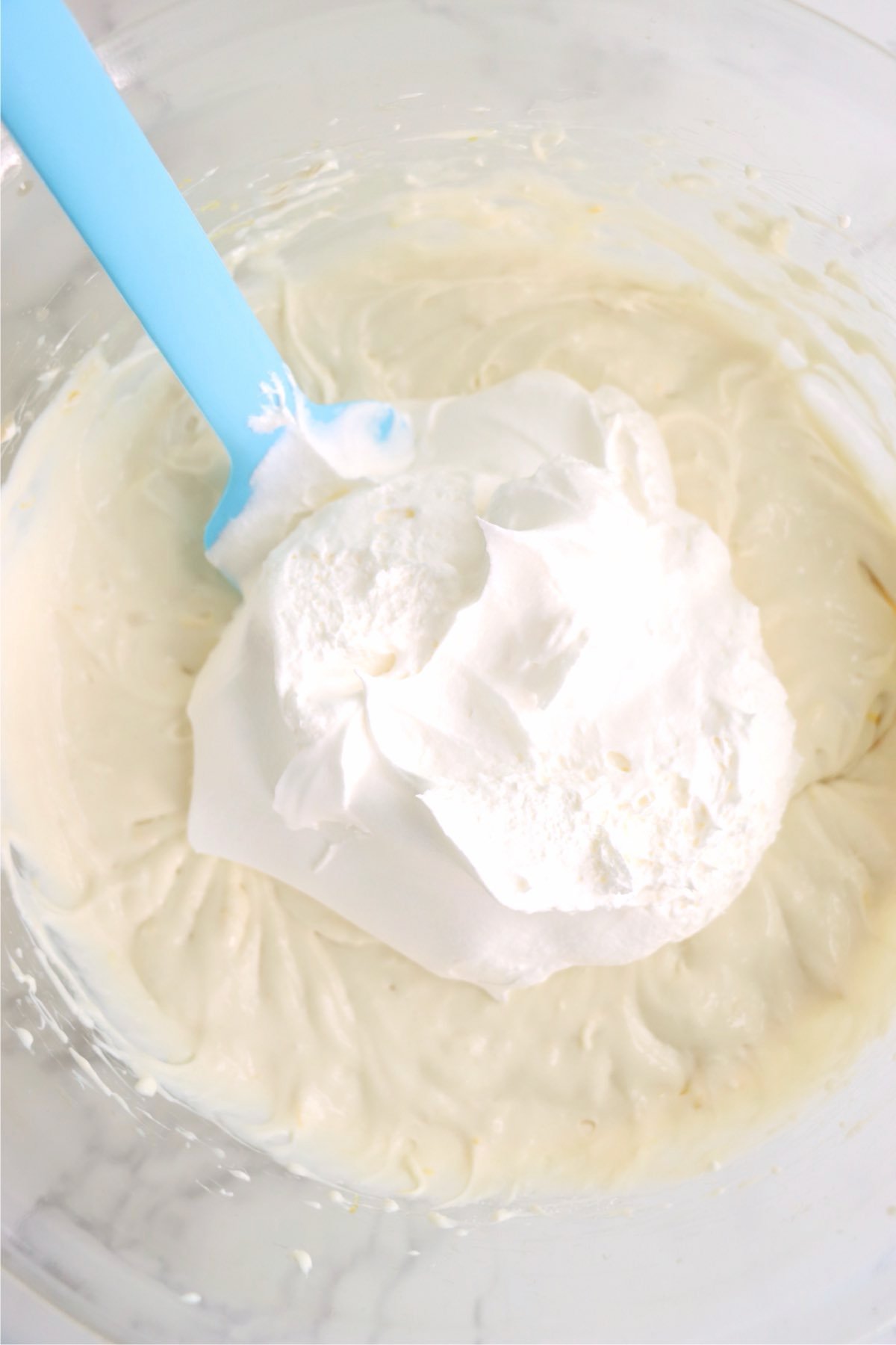 Whipped topping being folded into the cream cheese mixture with a blue spatula.