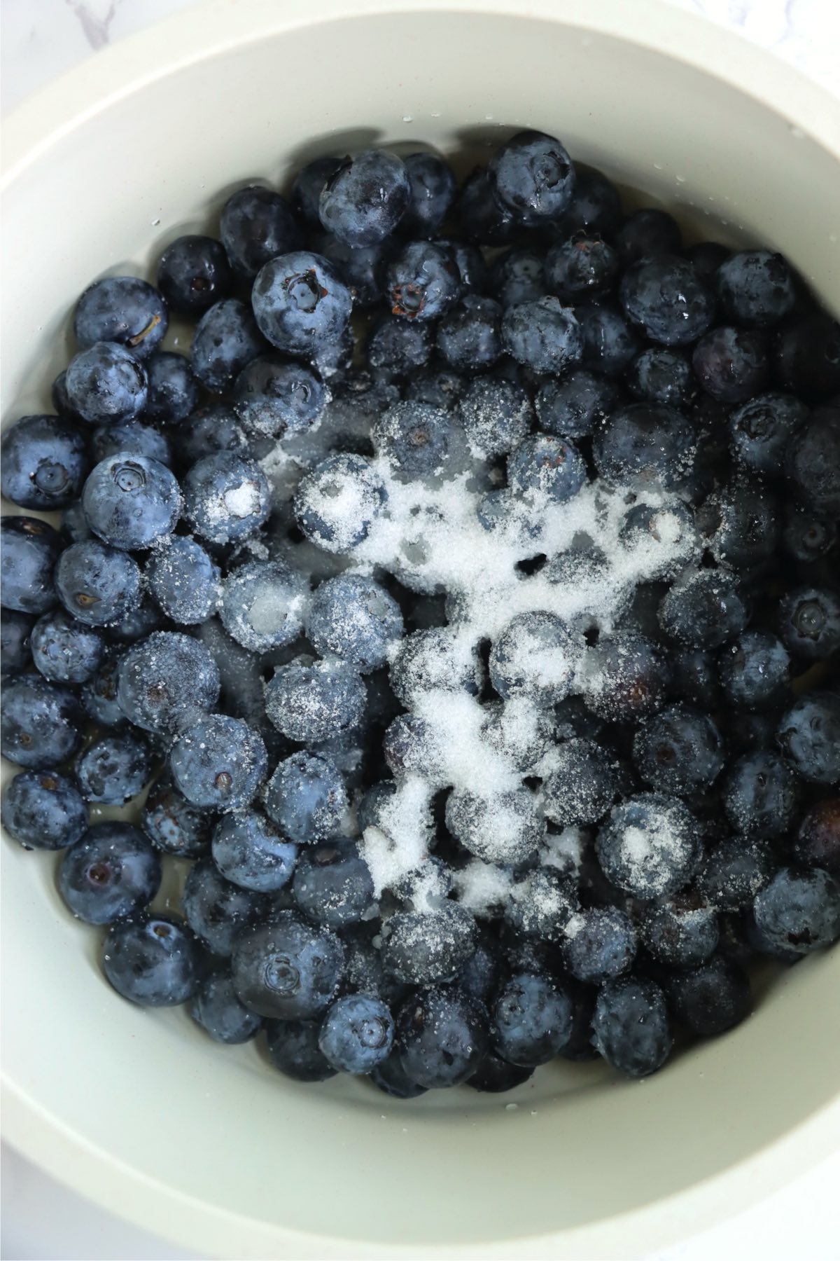 Fresh blueberries and granulated sugar in a white saucepan.