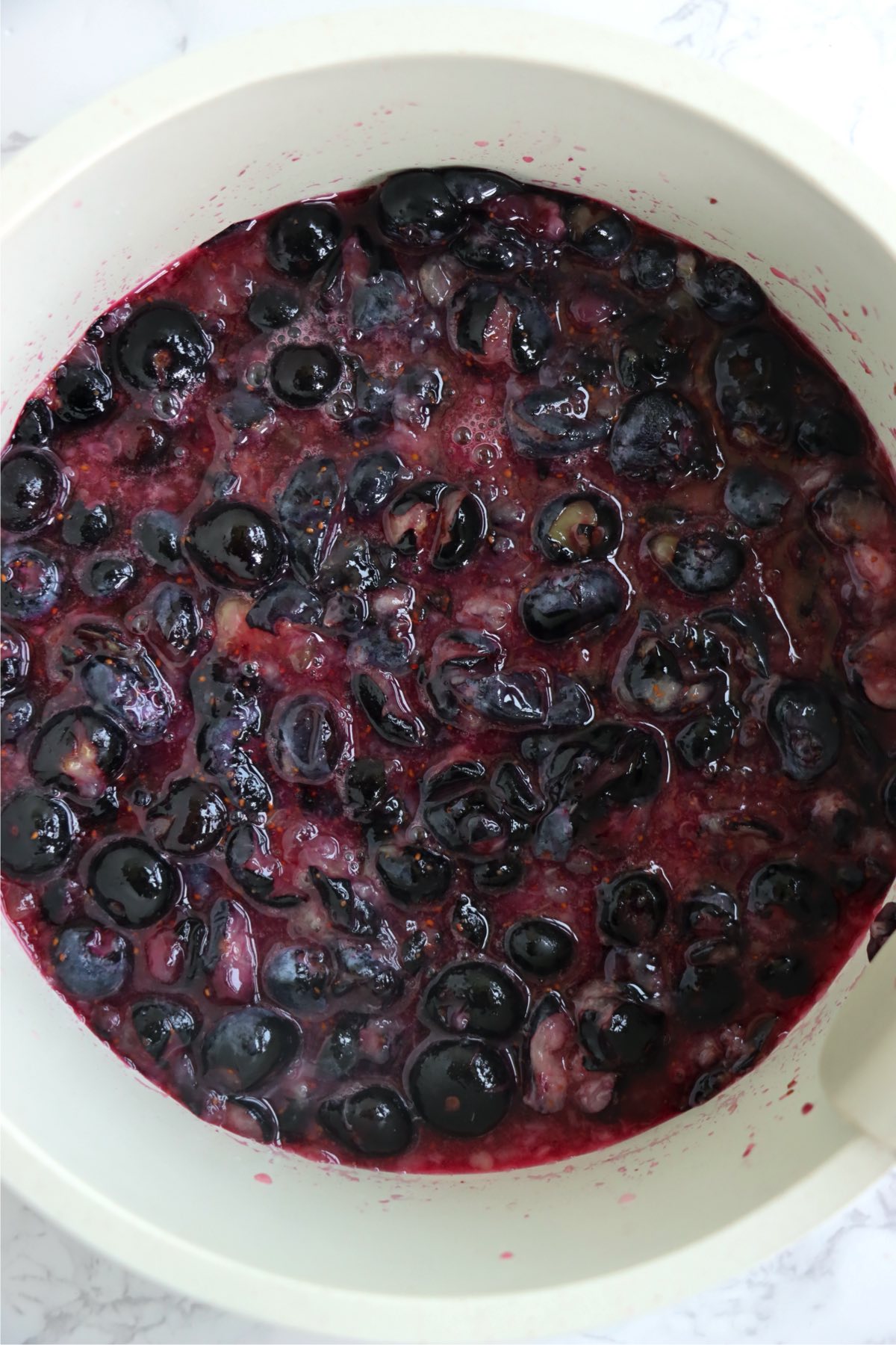 Cooked blueberry mixture with crushed berries in a white saucepan.