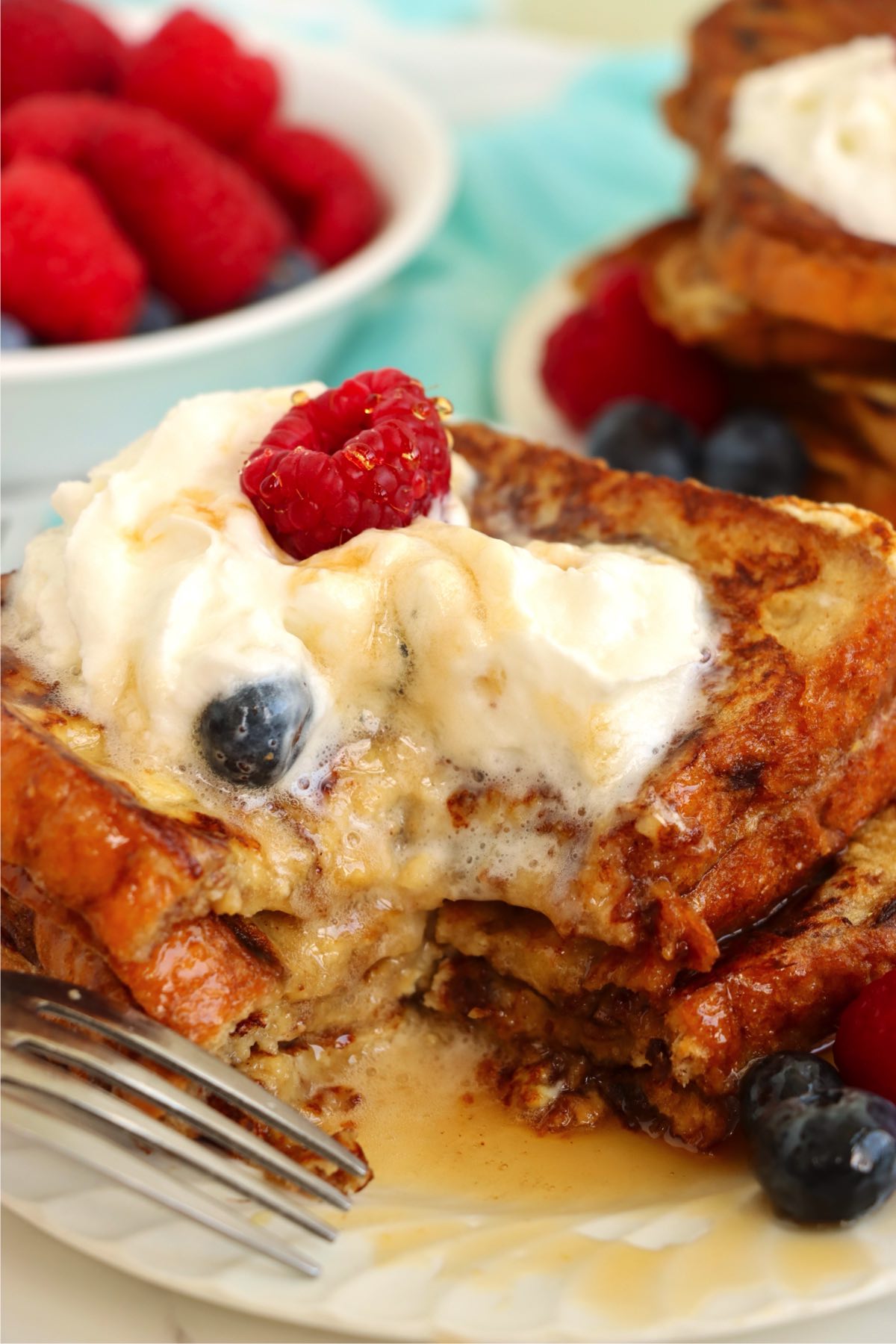 Slice of French toast cut open, showing fluffy inside with whipped cream, syrup, and fresh berries on top.
