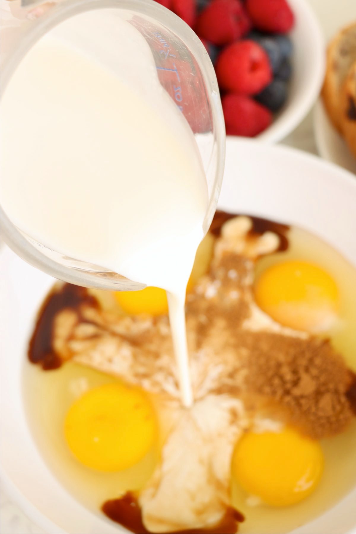 Cream being poured into a bowl with eggs, cinnamon, and vanilla.