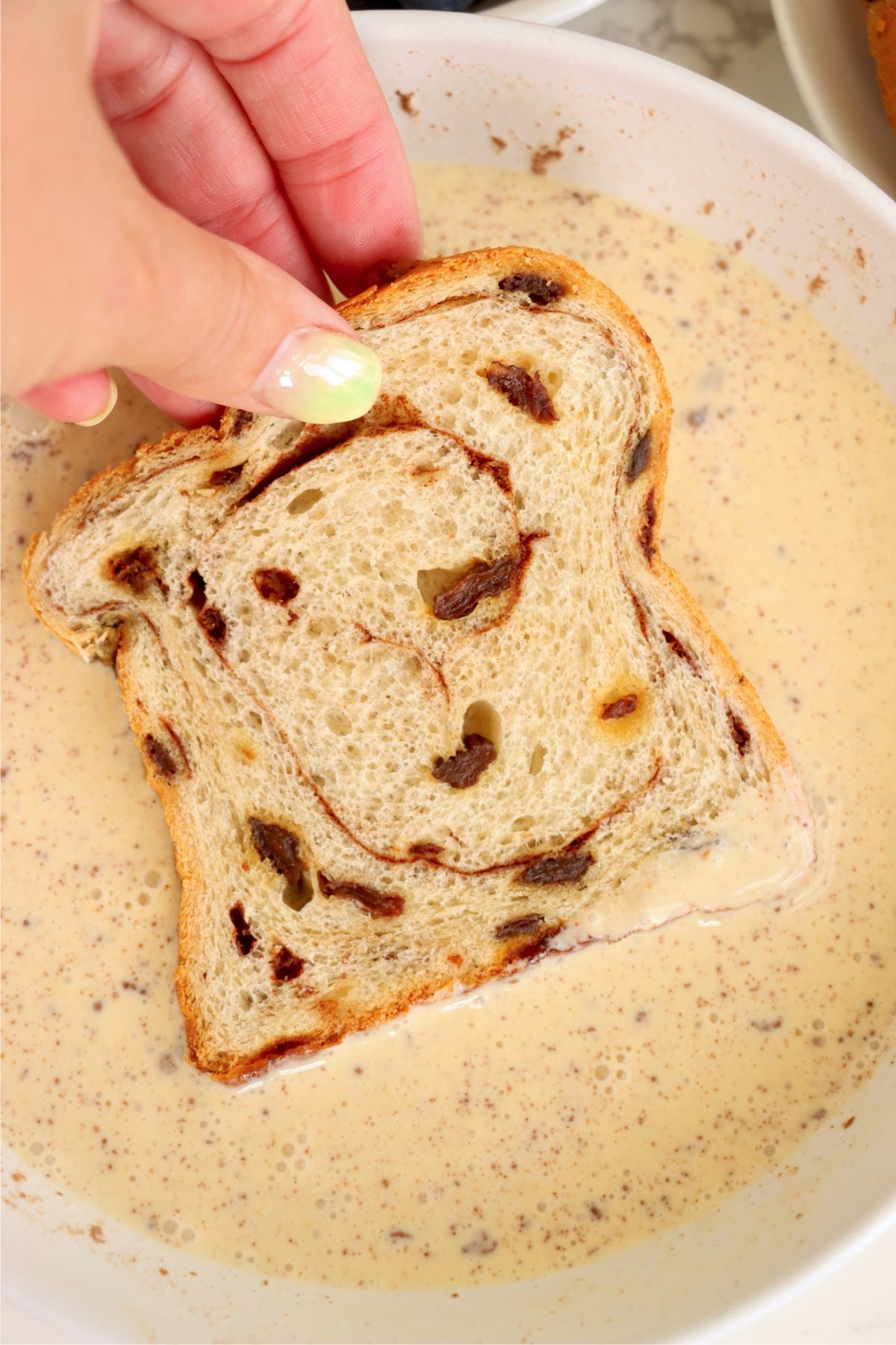 A slice of cinnamon swirl bread being dipped into the egg mixture.