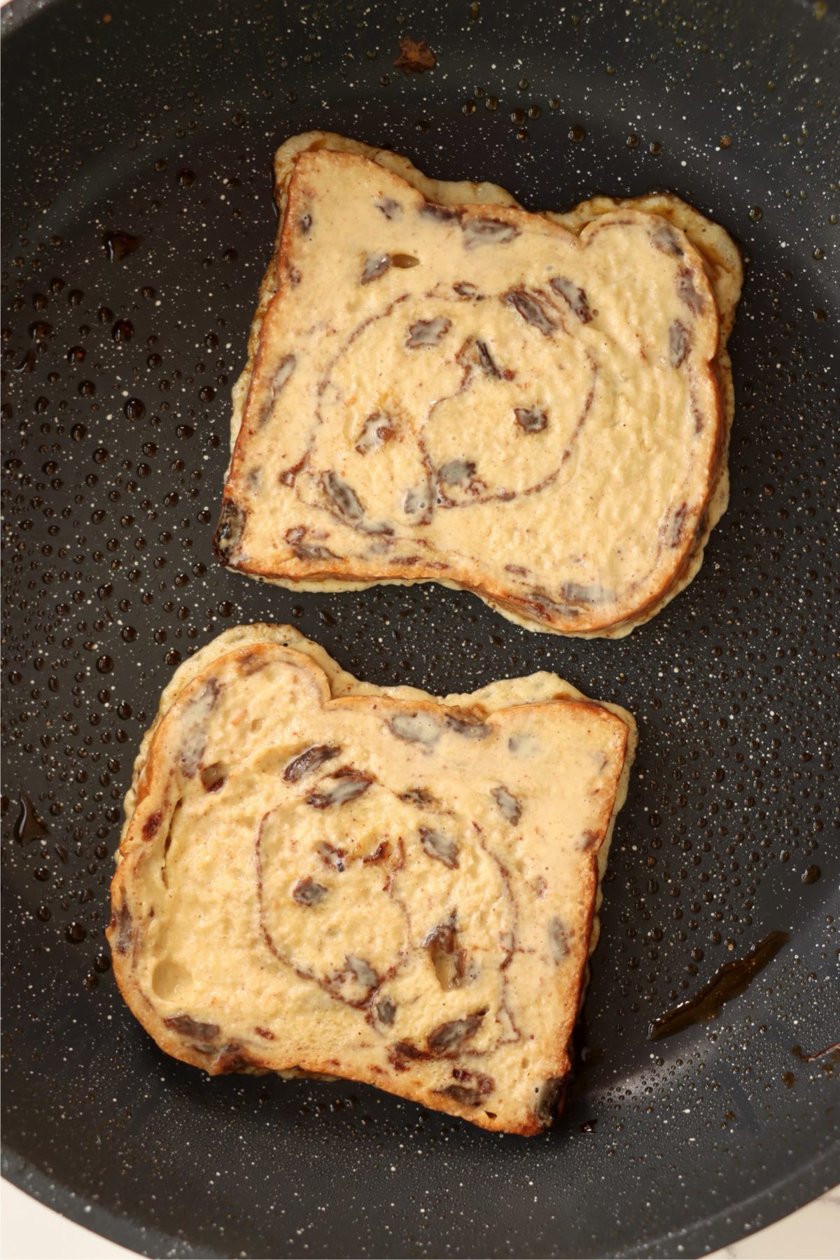 Two slices of dipped bread cooking in a skillet.