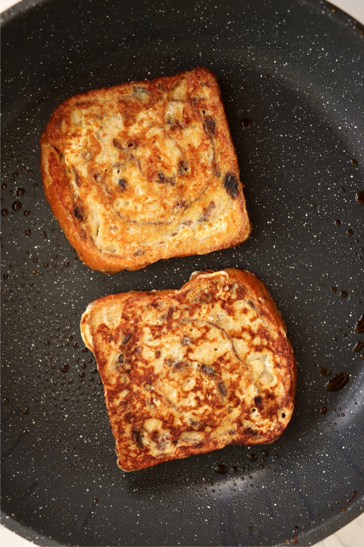 Two slices of French toast browning in a skillet.