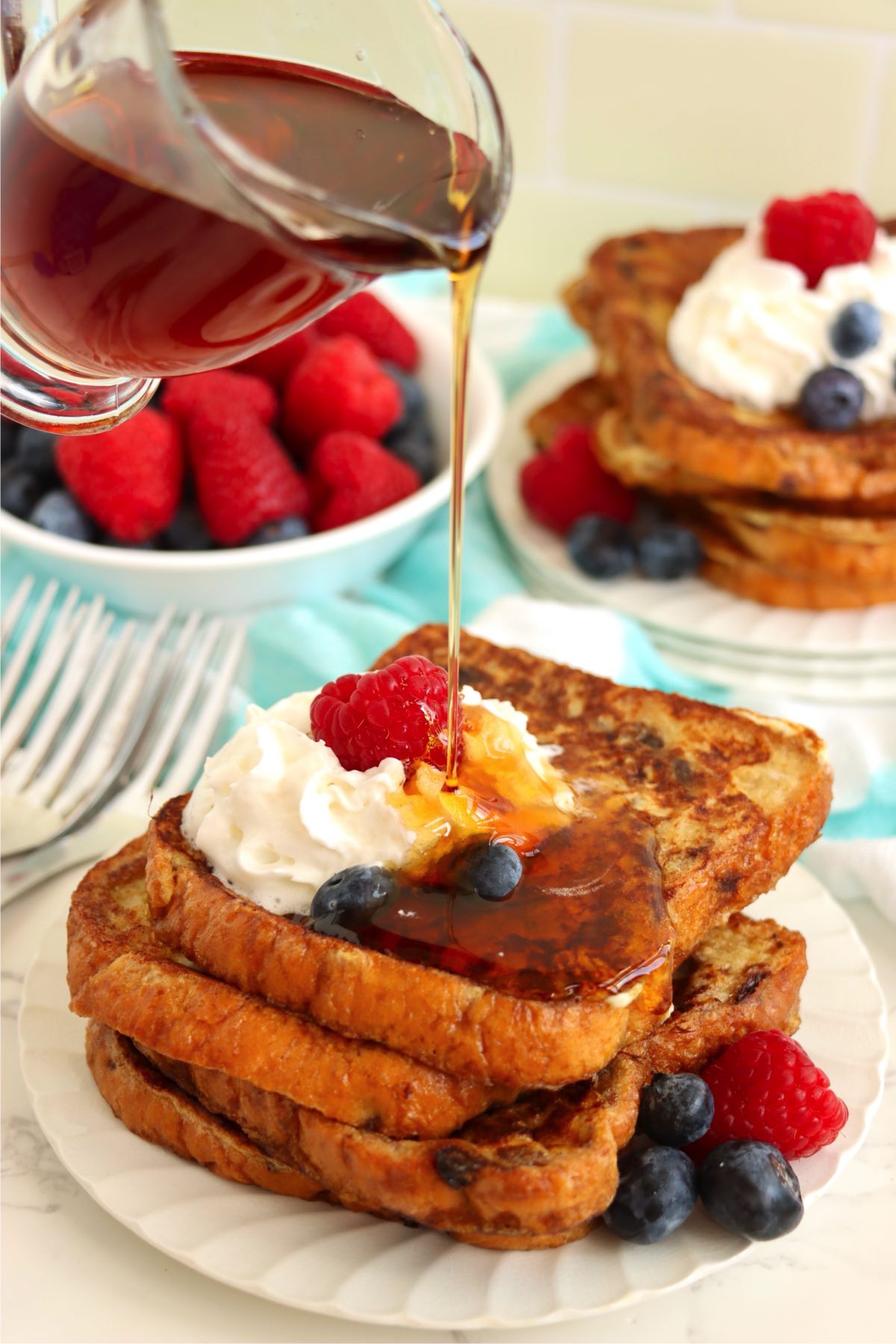 Syrup being poured over French toast with berries and whipped cream.