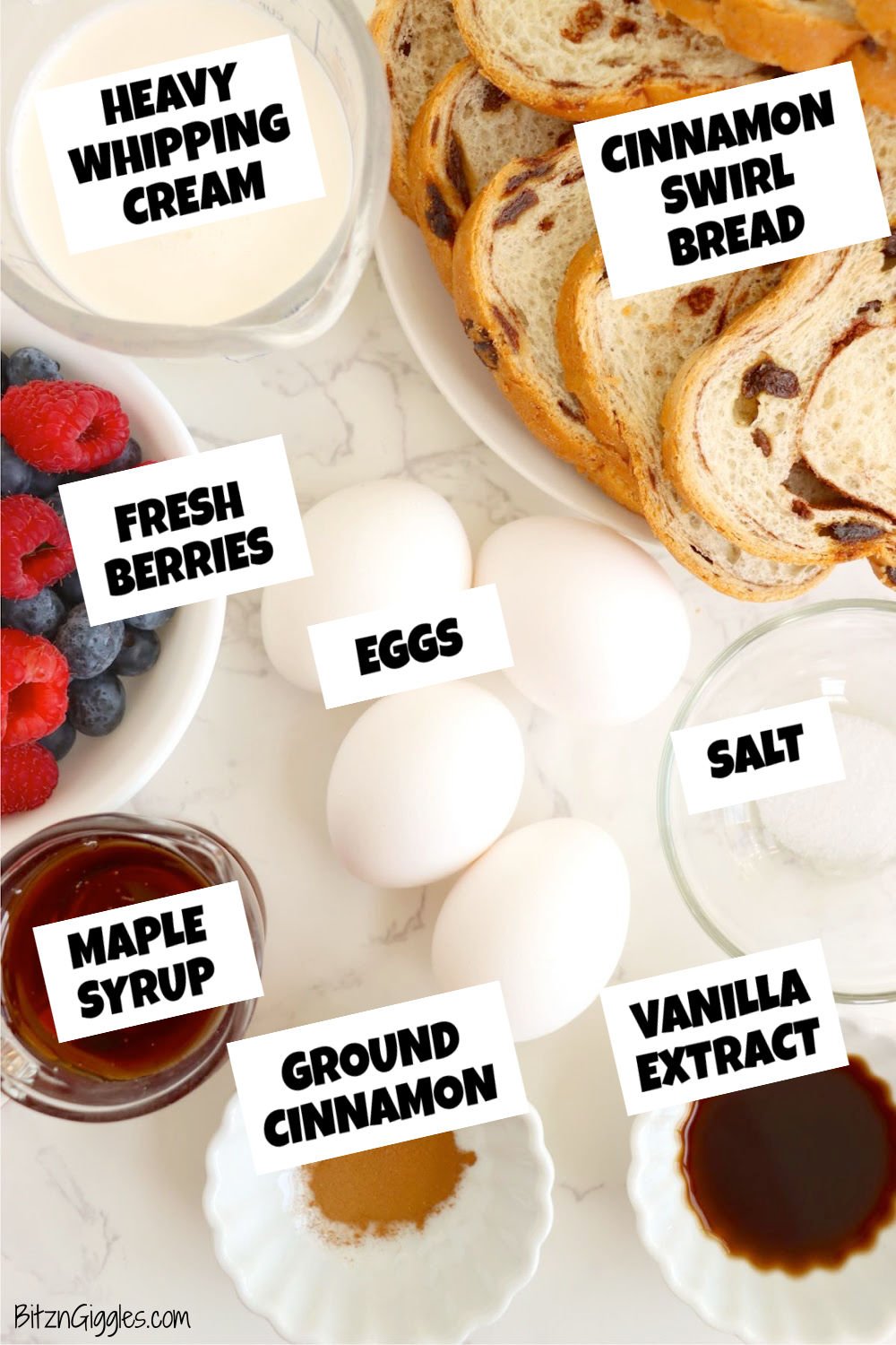 Overhead view of ingredients including cinnamon swirl bread, eggs, heavy cream, vanilla, cinnamon, salt, maple syrup, and fresh berries.