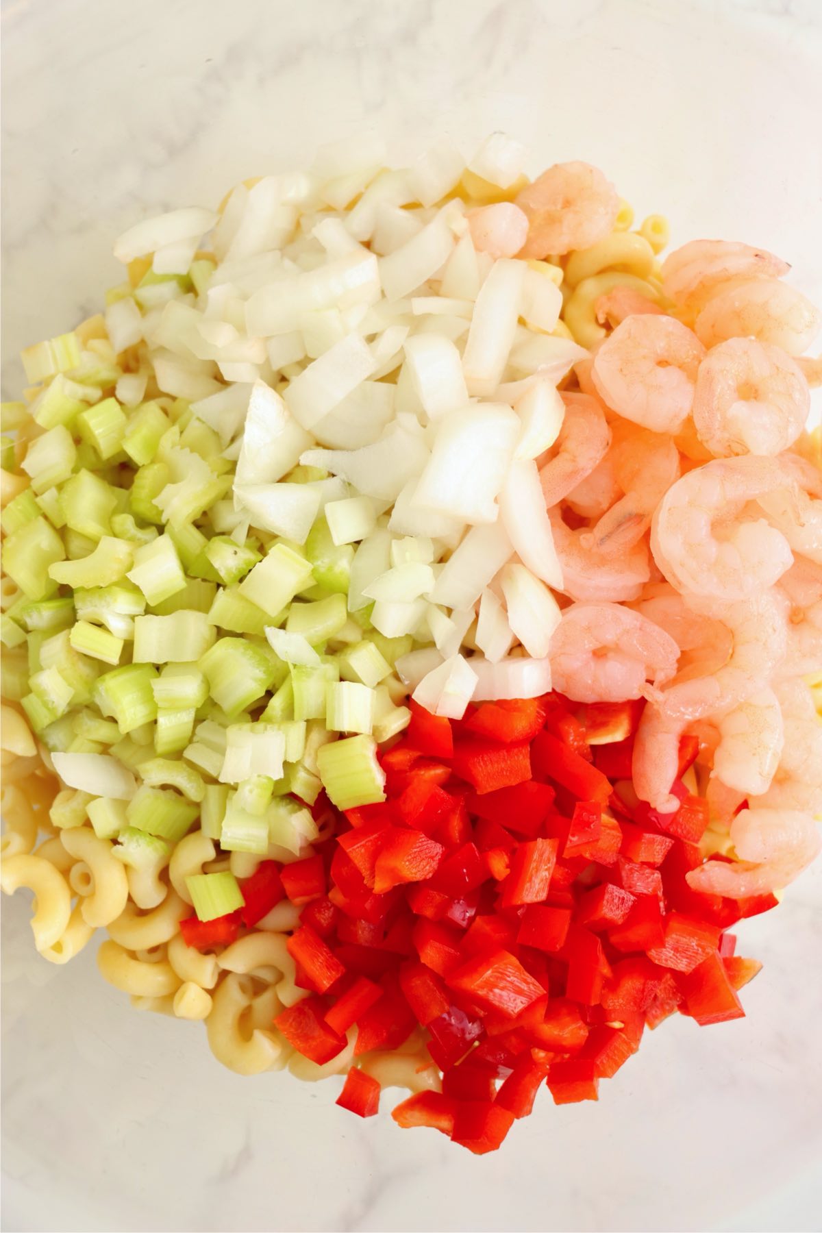 Chopped celery, onion, peppers, and shrimp on top of cooked pasta in a mixing bowl.