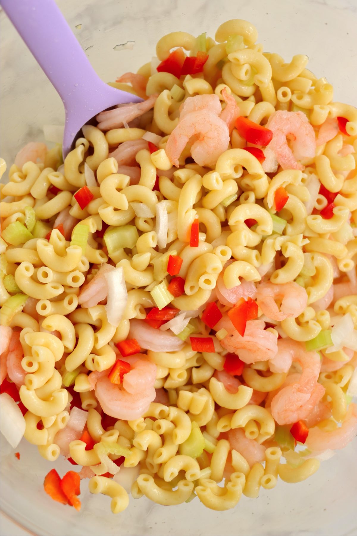 Pasta, shrimp, and chopped vegetables mixed together with a spoon.