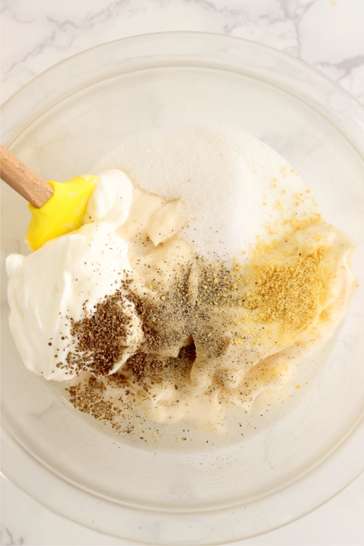 Dressing ingredients including mayonnaise, sour cream, sugar, celery seed, mustard, salt, and pepper in a mixing bowl.