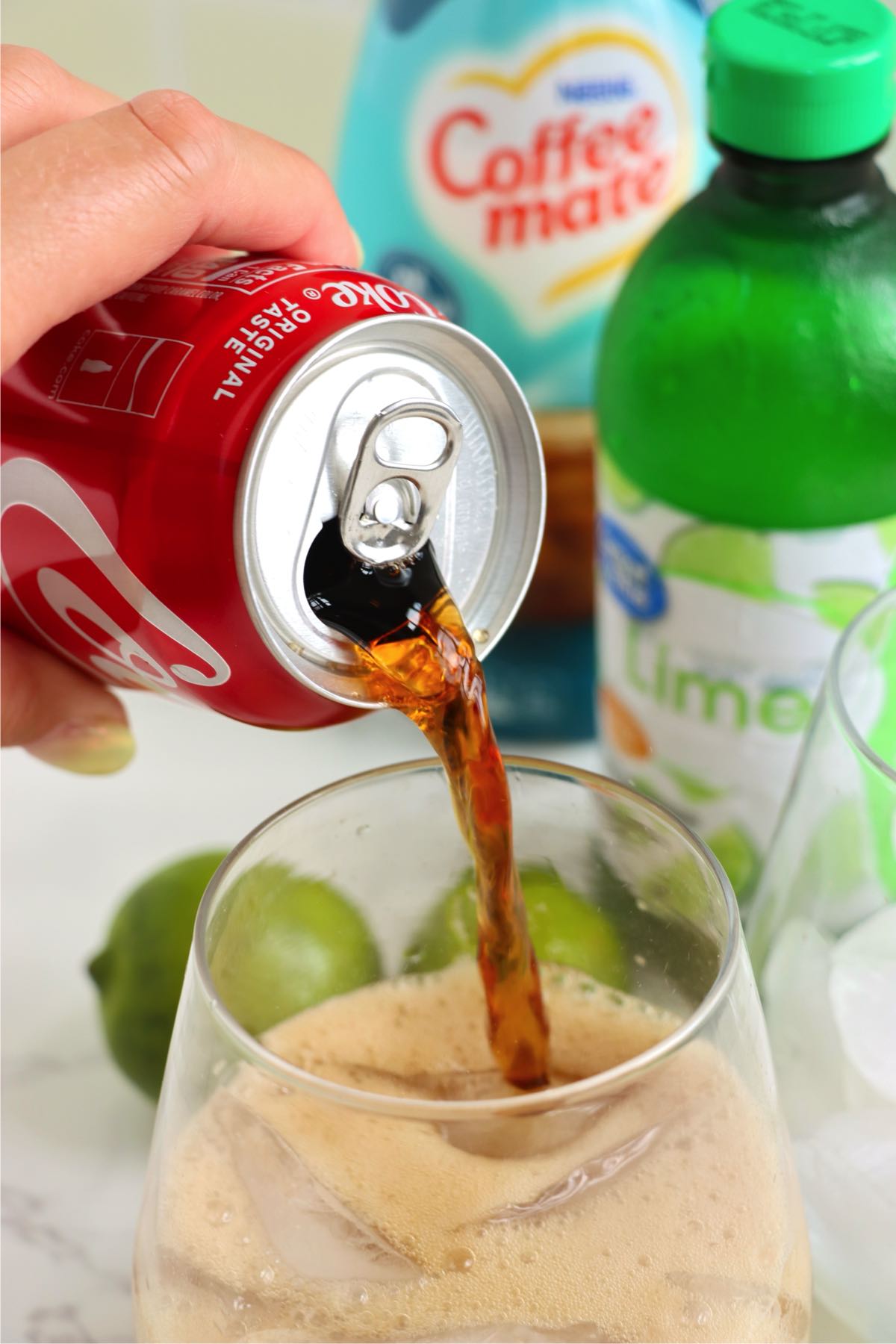 Pouring cola into a glass with lime juice and ice.