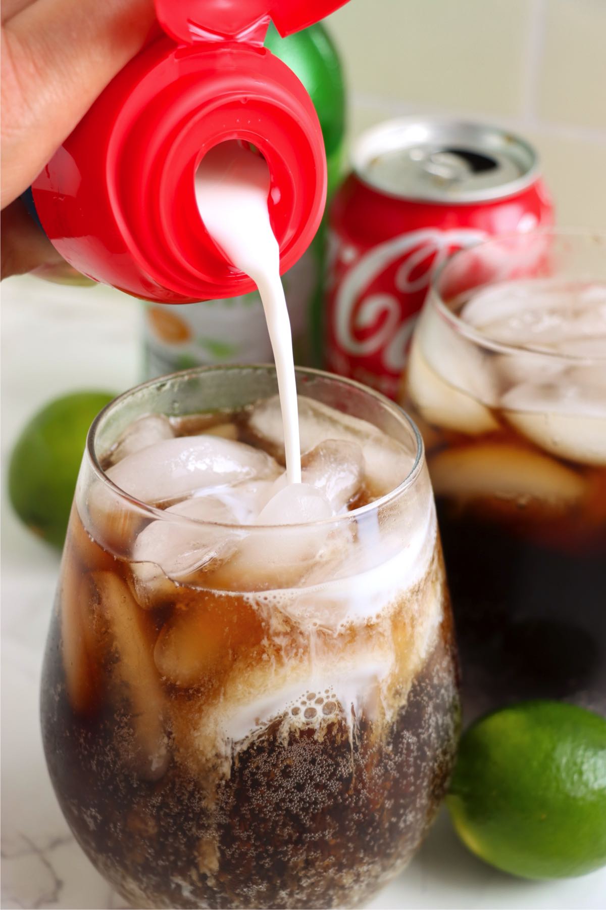 Adding coconut creamer to a glass of cola and lime over ice.