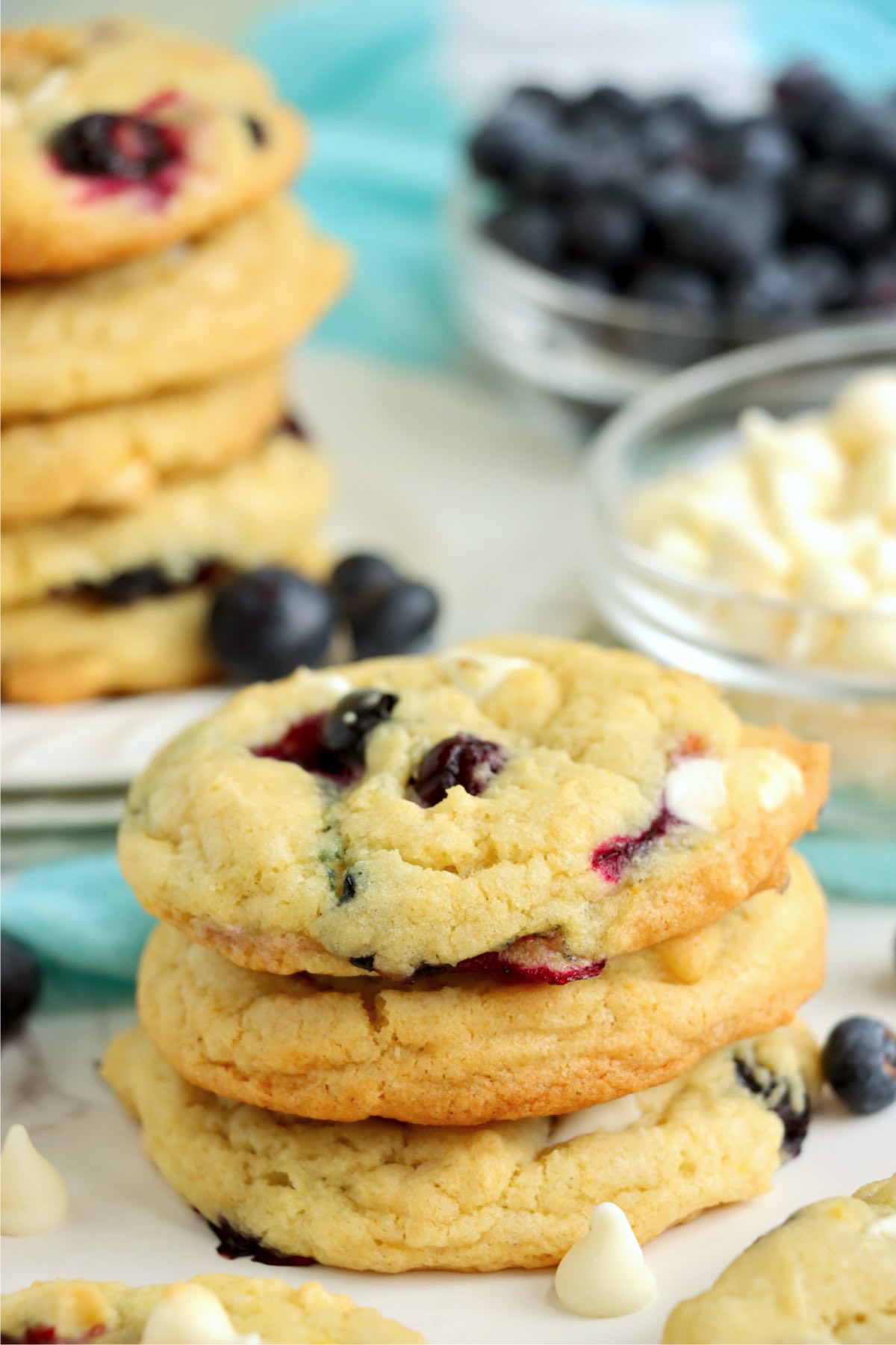 A small stack of golden cookies with blueberries and white chocolate chips, with fresh blueberries blurred in the background.
