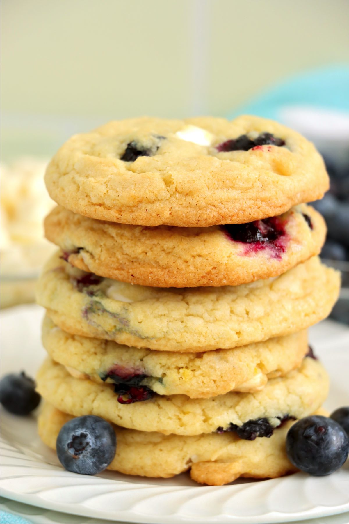 A tall stack of blueberry cookies on a plate with whole blueberries scattered at the base.