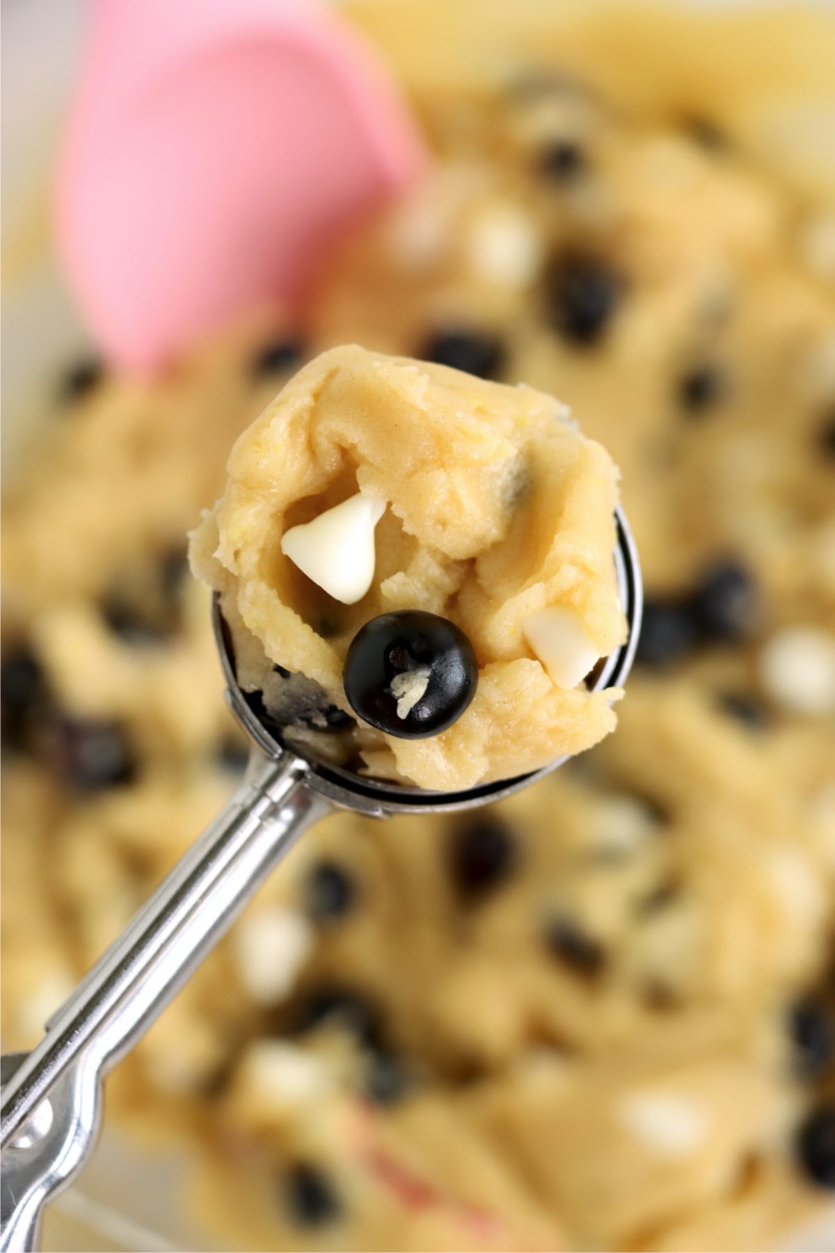 A cookie scoop holding a ball of dough with blueberries and white chocolate chips.